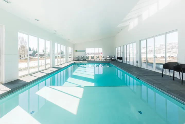Indoor swimming pool with full-height windows, a white ceiling, and dark-toned coping
