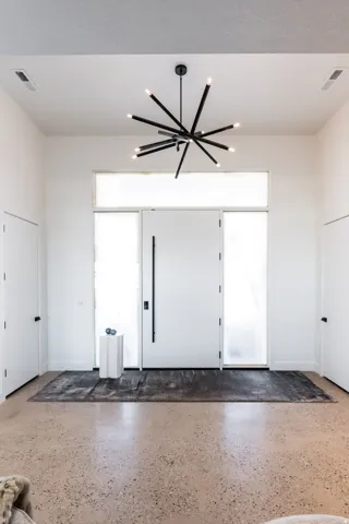 Entryway featuring a black modern sputnik chandelier, a white solid core entry door with a vertical pull handle, frosted sidelight windows, and polished concrete flooring