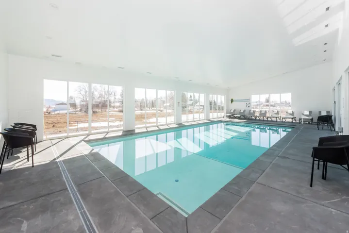 Indoor swimming pool featuring a bright white interior, extensive window walls, recessed lighting, and a durable perimeter deck
