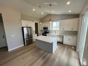 Modern kitchen featuring wood-finish flooring, white cabinetry, a central island, stainless steel appliances, and a vaulted ceiling with recessed lighting