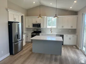 Kitchen featuring a central island with countertop seating, white shaker cabinetry, stainless steel appliances, and wood-finish flooring