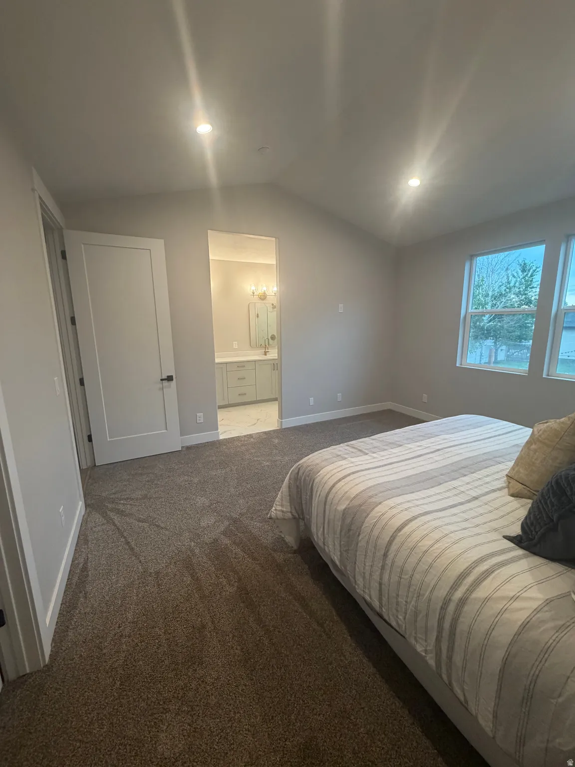 Spacious bedroom with vaulted ceiling, recessed lighting, and soft carpeting