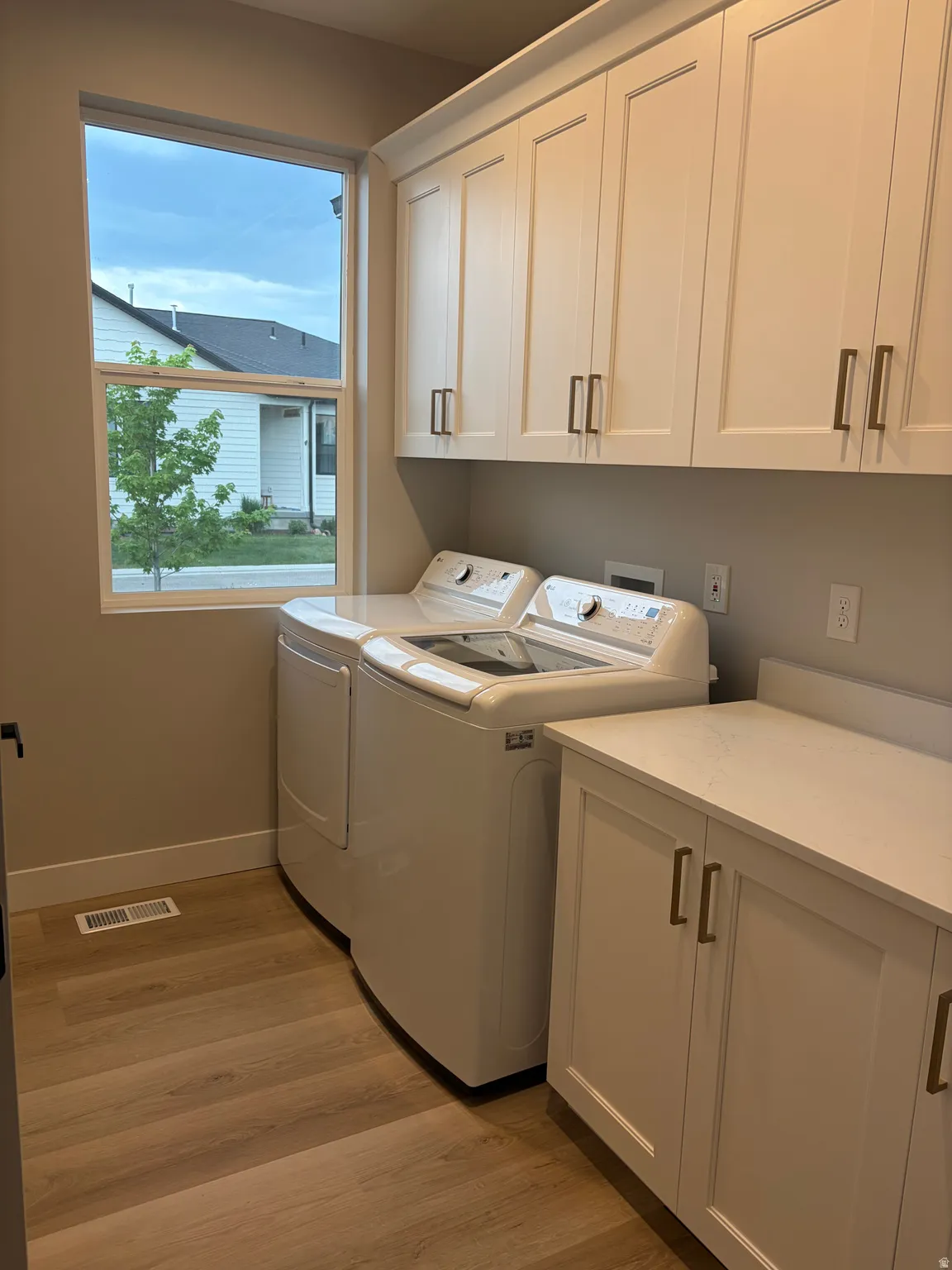 Laundry room featuring white shaker-style cabinetry, a built-in counter, wood-finish flooring, and a large window