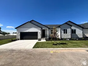Contemporary exterior featuring a white siding and stone façade, black trim, a dark garage door, and a manicured lawn with a young tree
