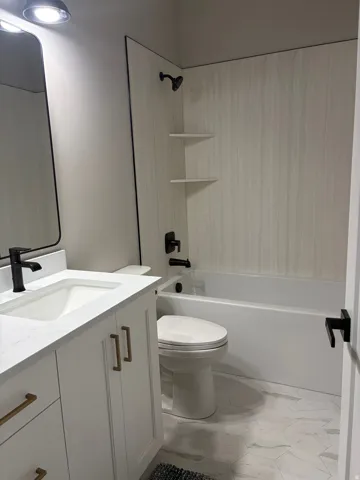 Bathroom featuring a white vanity with gold-tone hardware, a white countertop with an integrated sink, and matte black plumbing fixtures