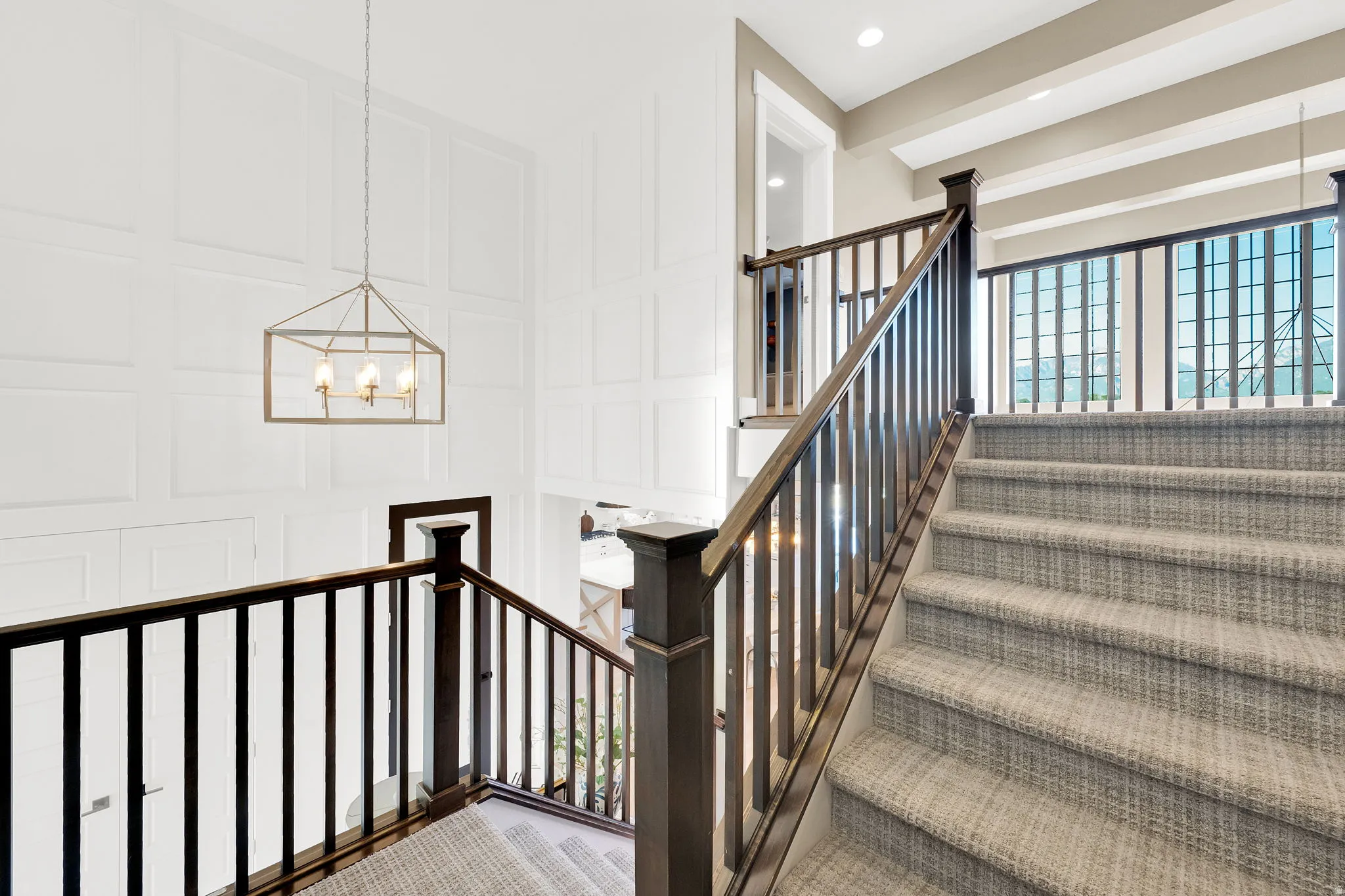 Staircase featuring dark wood handrails, light gray patterned carpeting, and white paneled walls