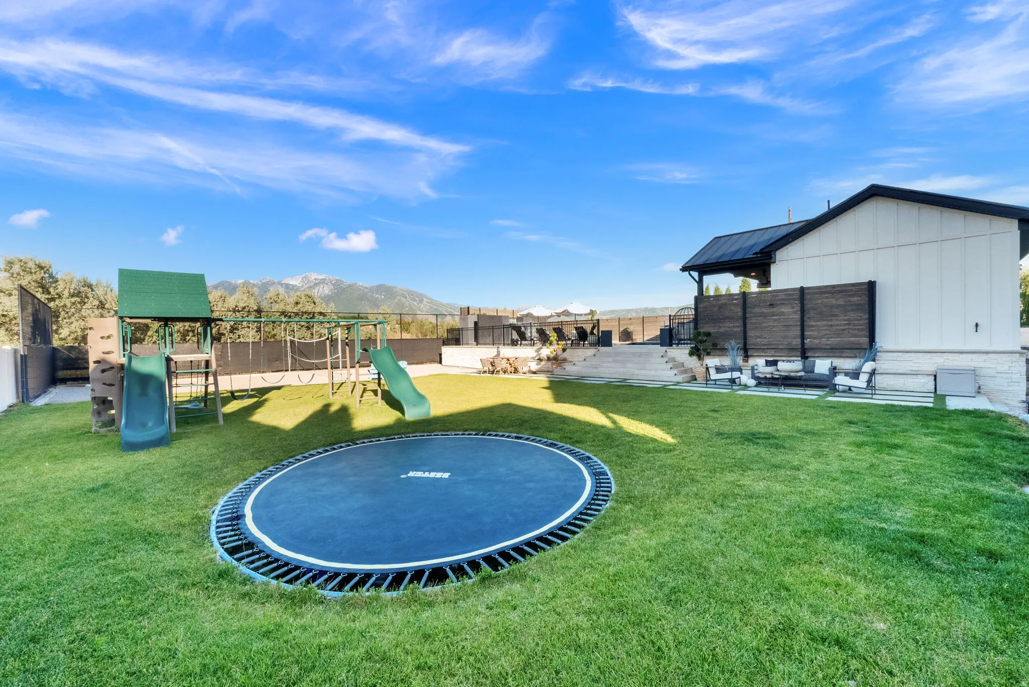 Expansive green lawn with a built-in trampoline, play structure, and adjacent patio seating