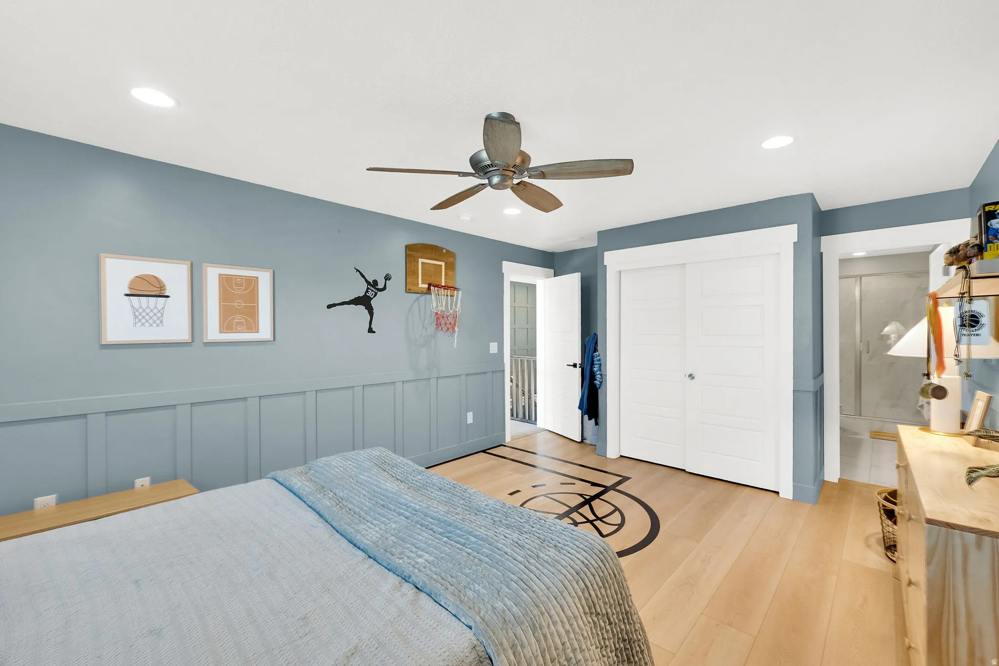 Light wood-finish flooring with an integrated graphic, ceiling fan, recessed lighting, and board and batten wall paneling