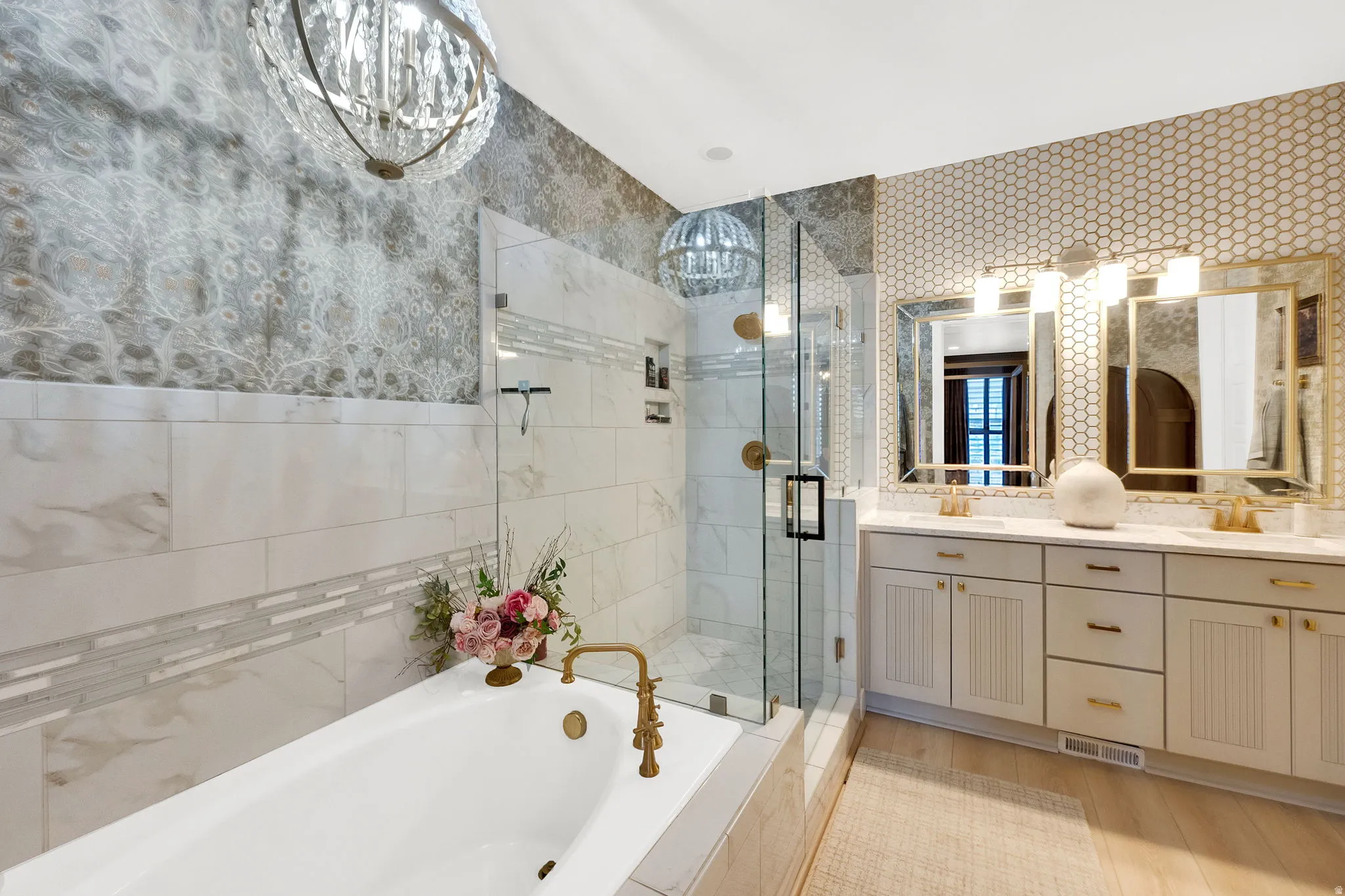 Bathroom featuring a built-in soaking tub with brass fixtures, a glass-enclosed shower, dual vanity with quartz countertops, and decorative wall tiling
