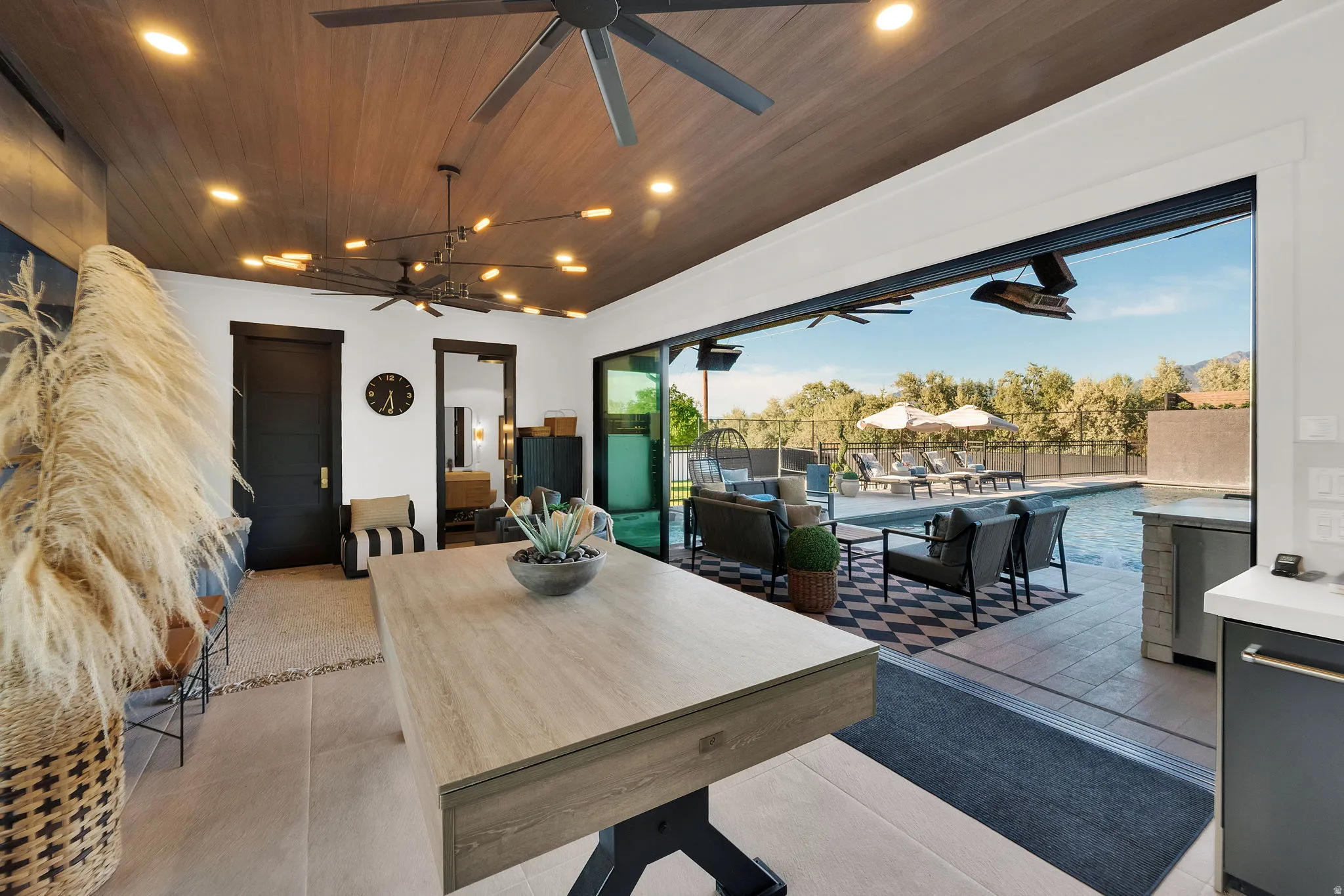 Expansive indoor-outdoor living space featuring a wood-finish ceiling with recessed lighting, large format tile flooring, and a full-width sliding glass door system
