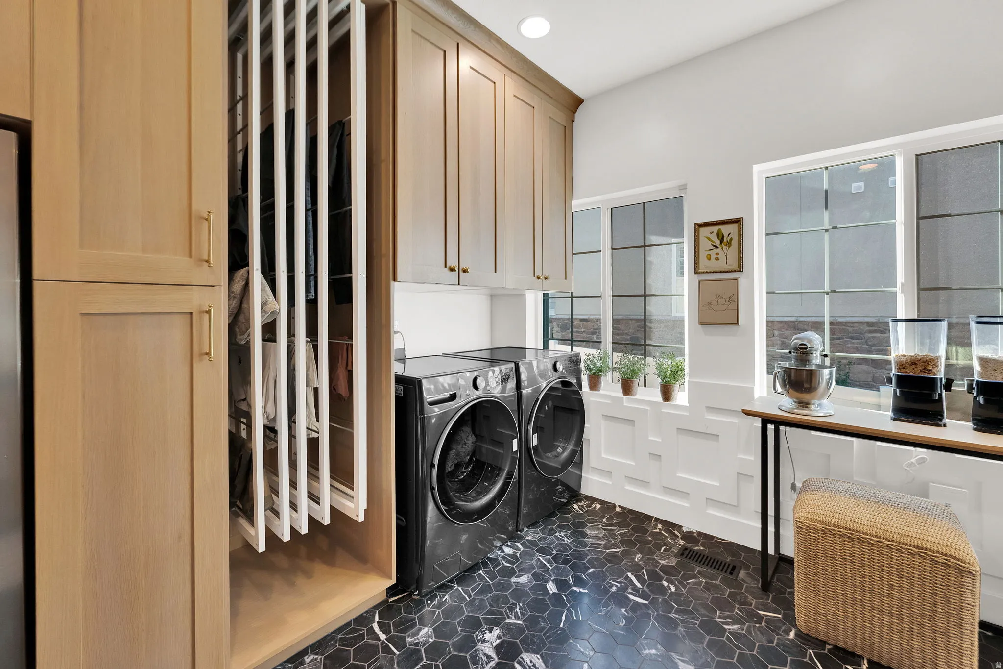 Laundry area featuring front-loading machines, black hexagonal tile flooring, and light wood-finish cabinetry