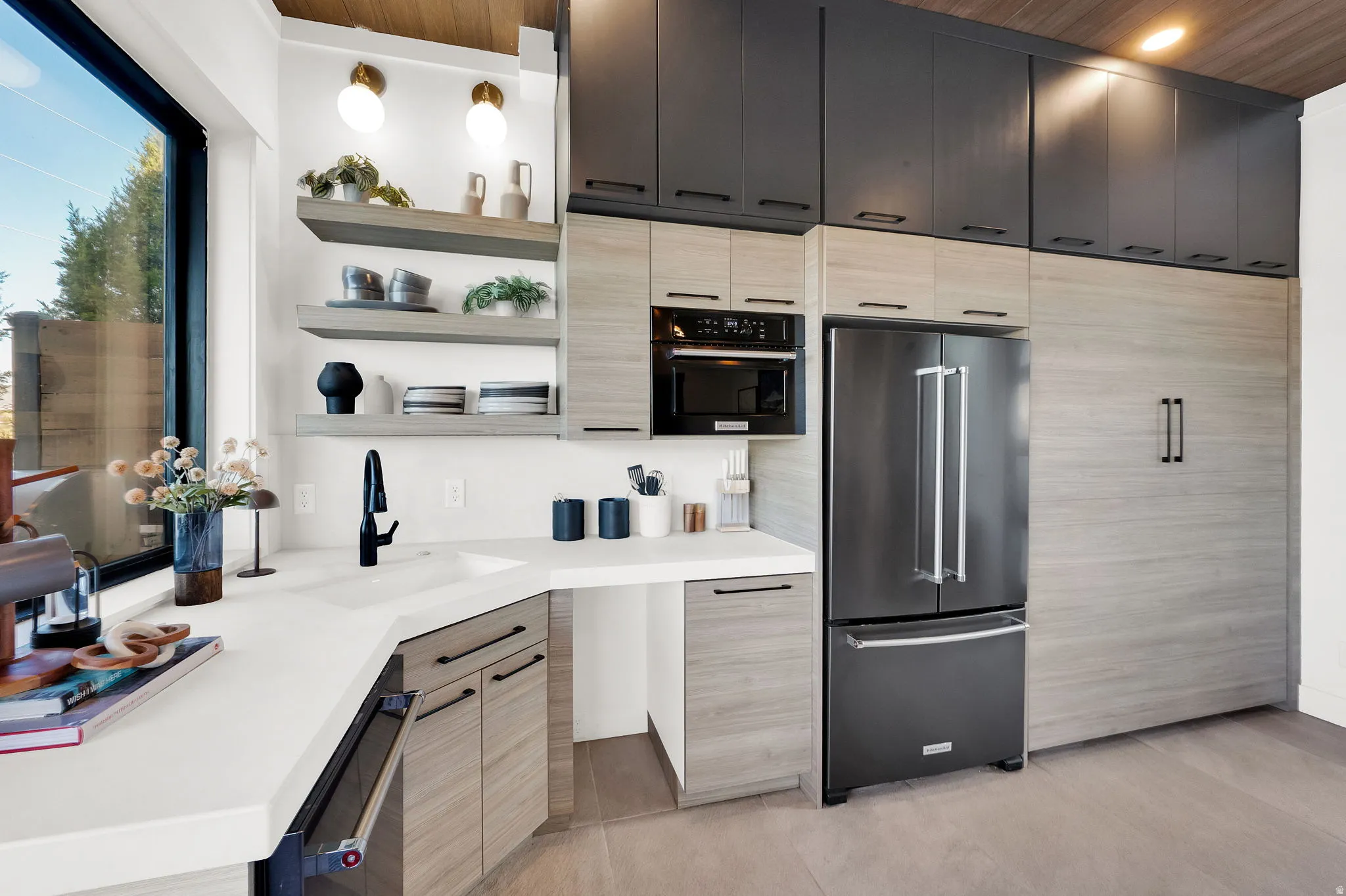 Modern kitchen featuring light wood-finish cabinetry, white countertops, built-in microwave, and a black stainless steel refrigerator