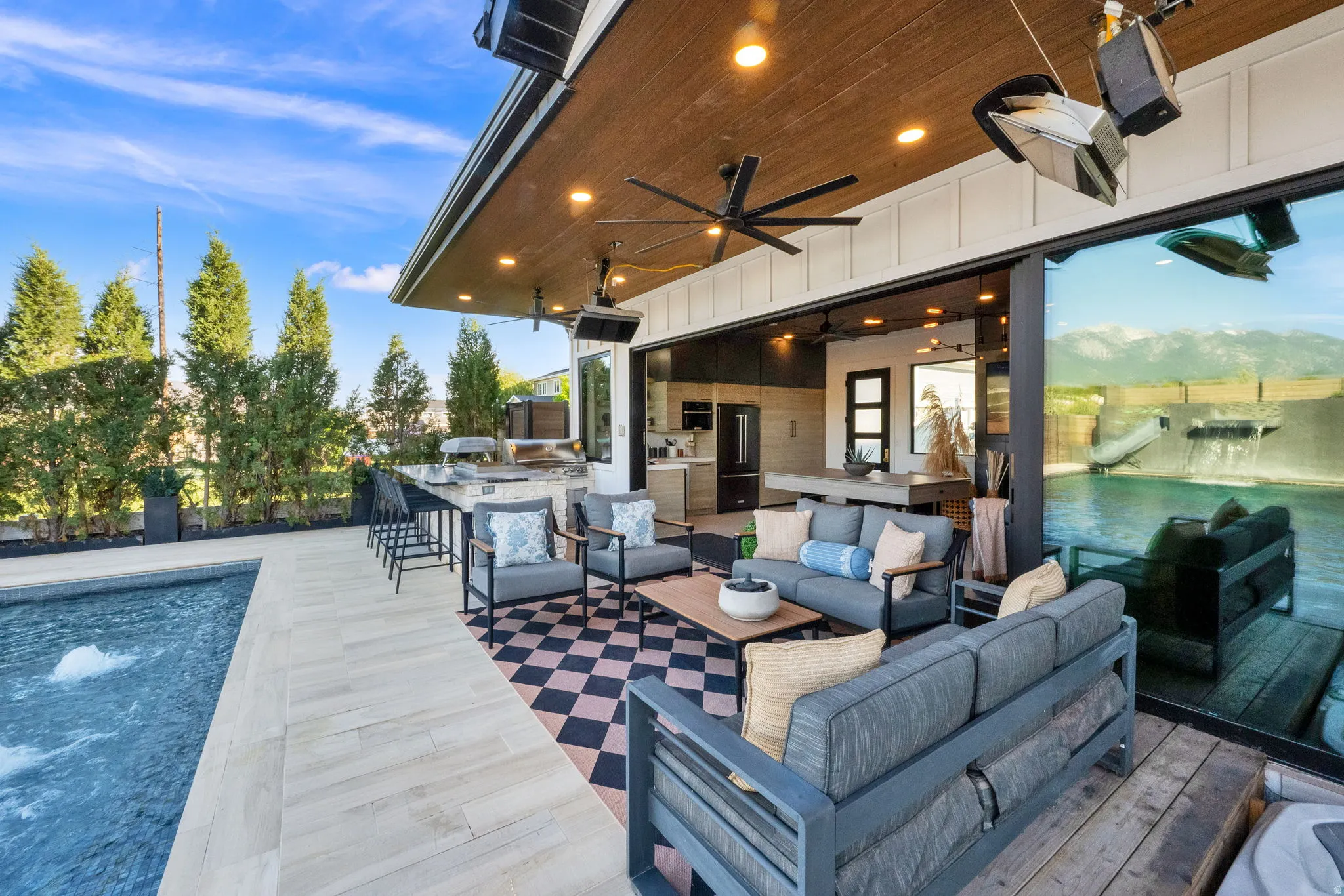 Covered patio featuring wood-finish ceiling with recessed lighting and ceiling fan, an outdoor kitchen with bar seating, and a checkered-pattern outdoor rug