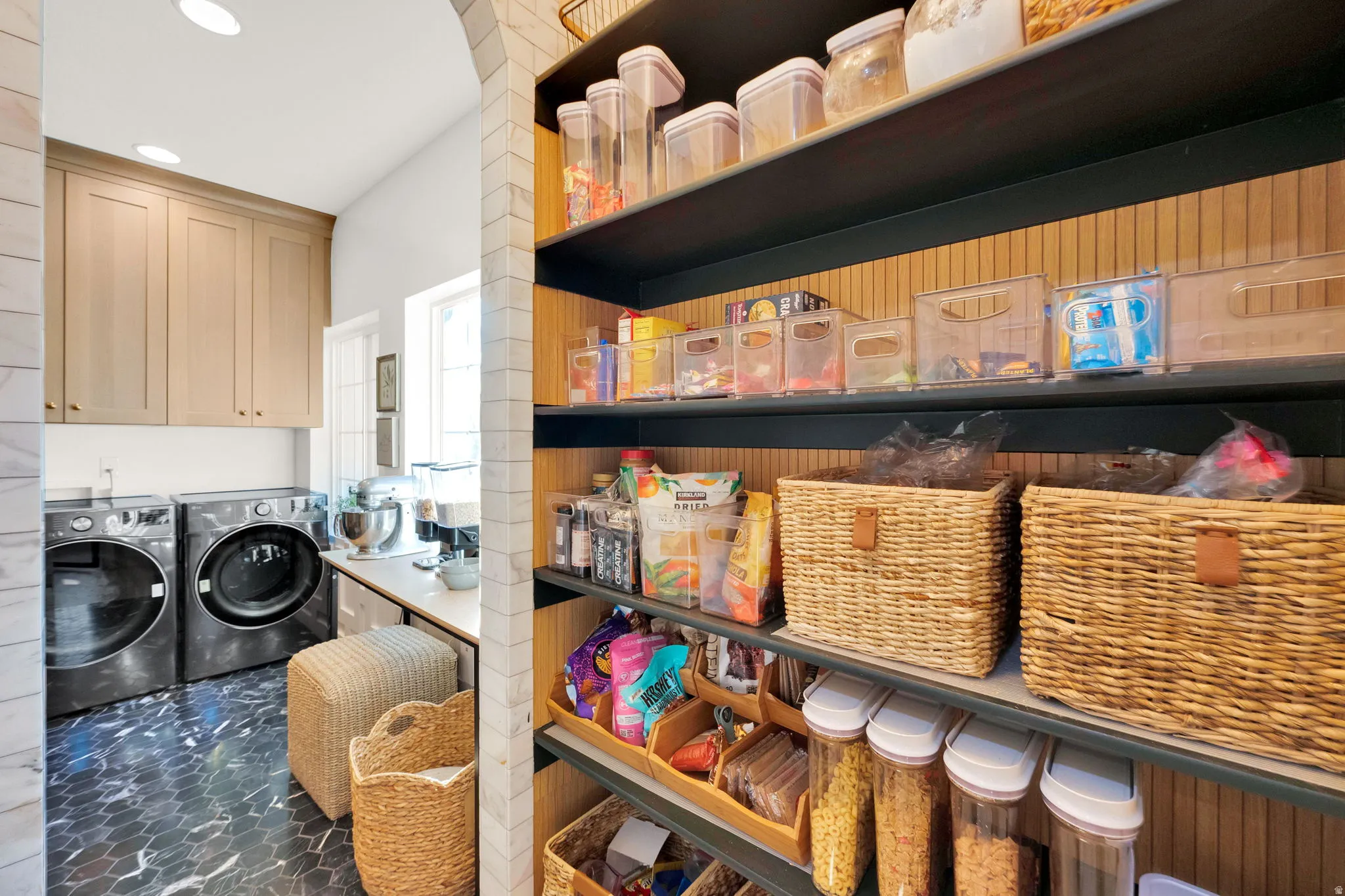 Dedicated laundry area with stone tile flooring and light-toned cabinetry