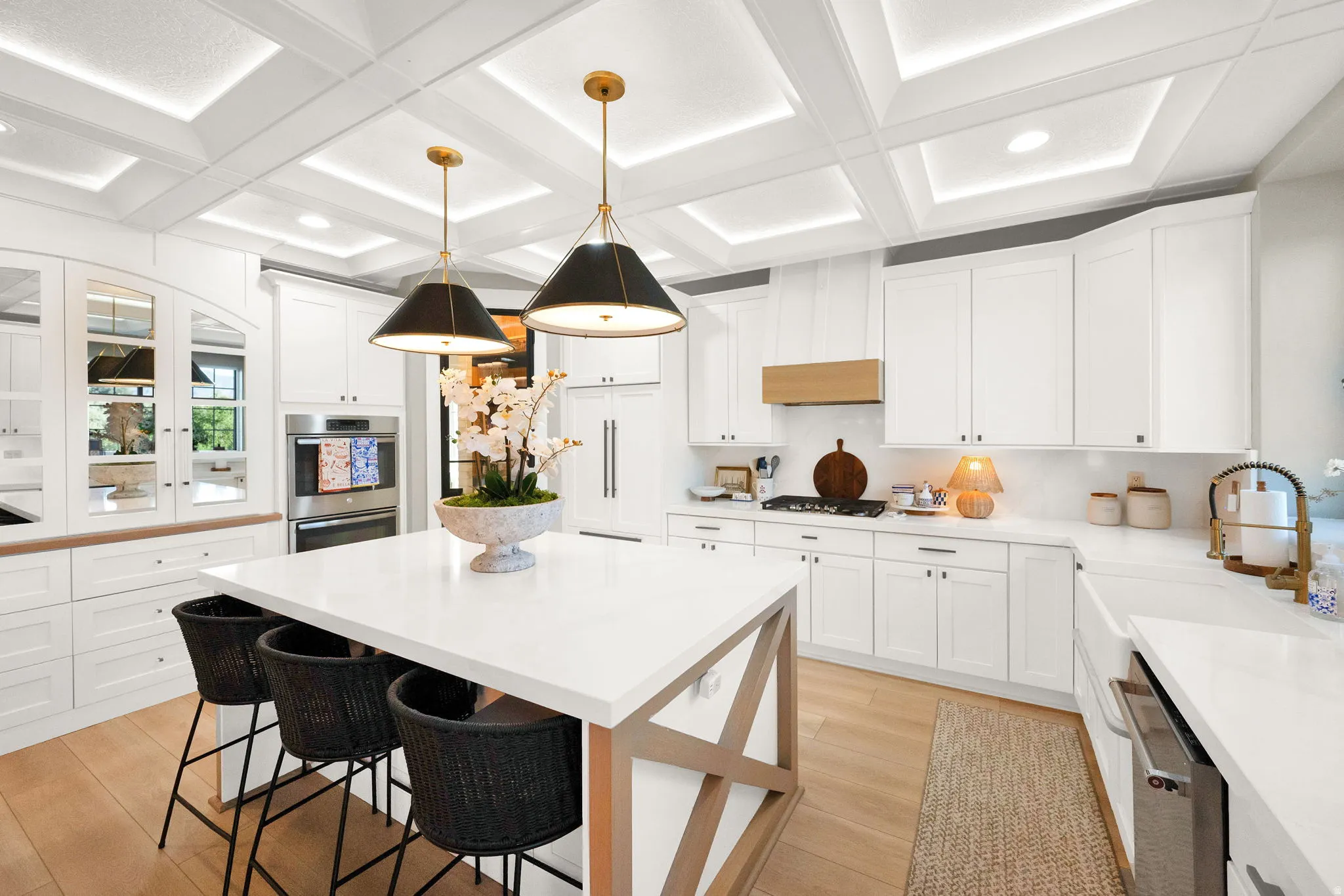 Modern kitchen featuring a large central island with seating, white shaker cabinetry, and wood-finish flooring