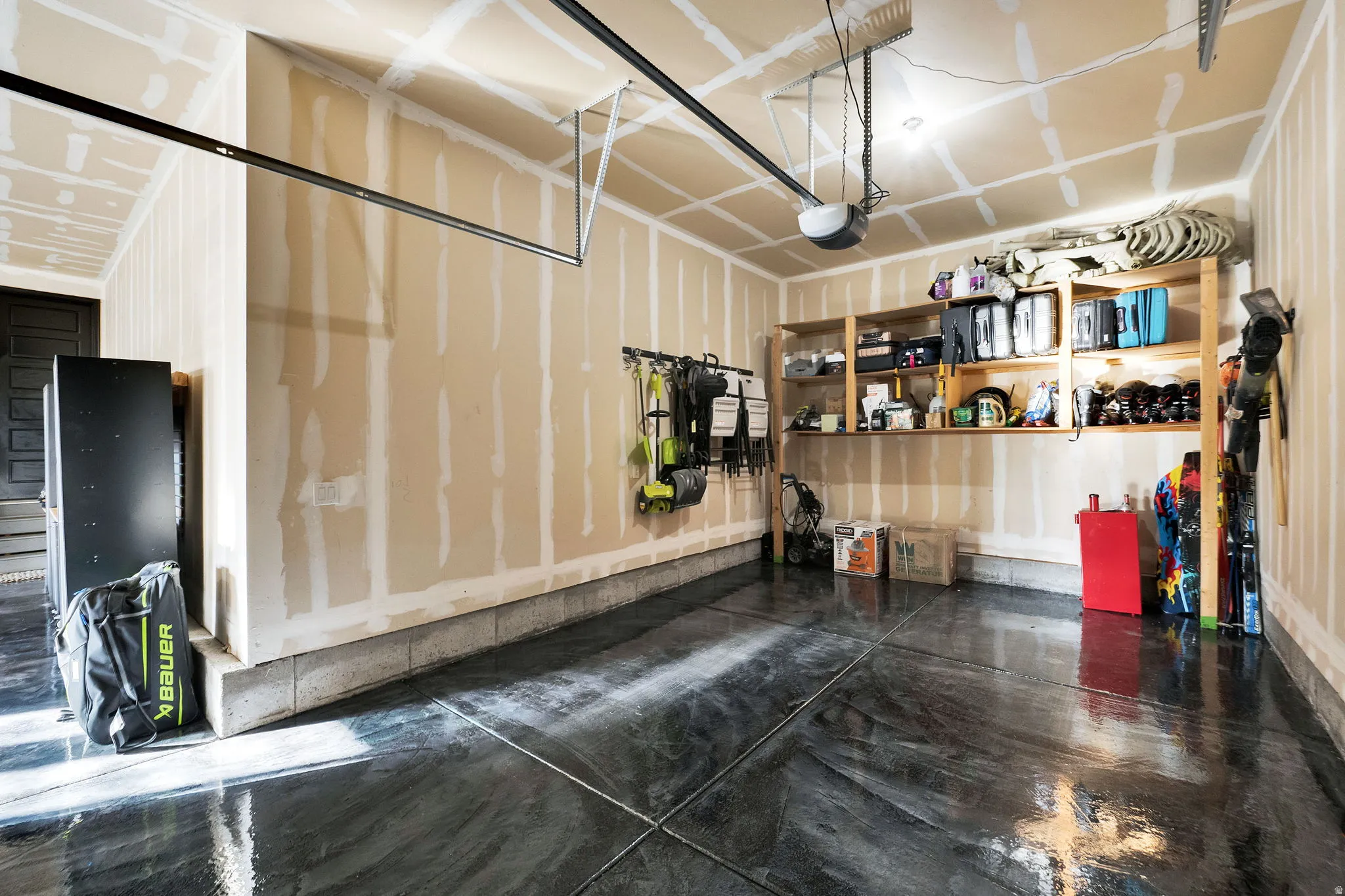 Garage featuring a reflective epoxy floor finish, built-in shelving, high ceilings, automatic garage door opener, and a side entrance door