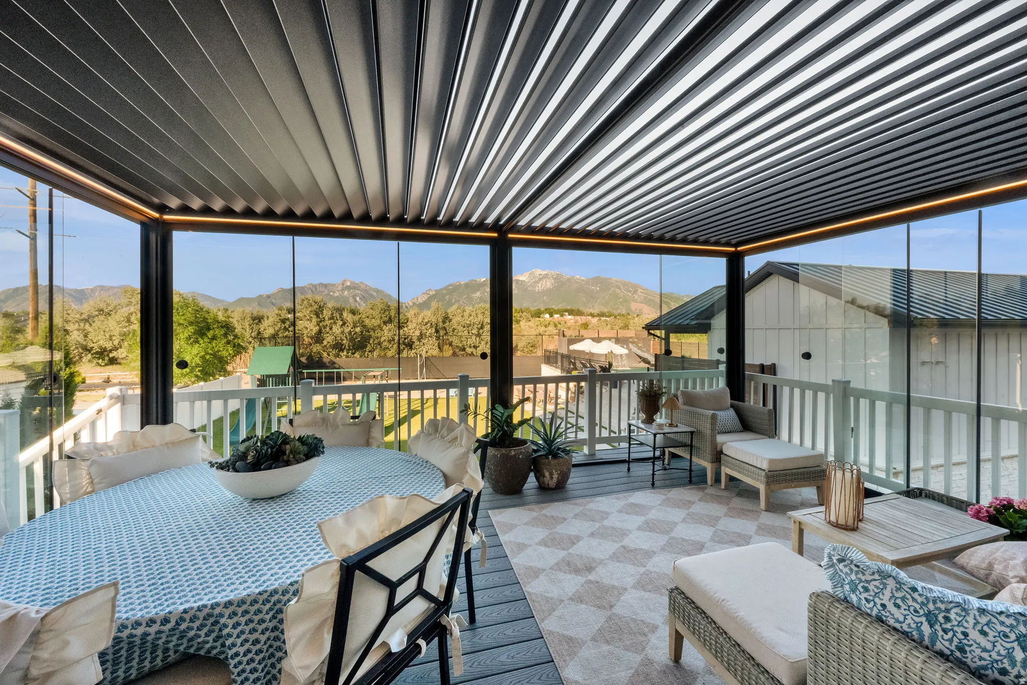 Enclosed outdoor living space featuring a louvered pergola ceiling with integrated lighting, glass panel walls, and a composite deck floor