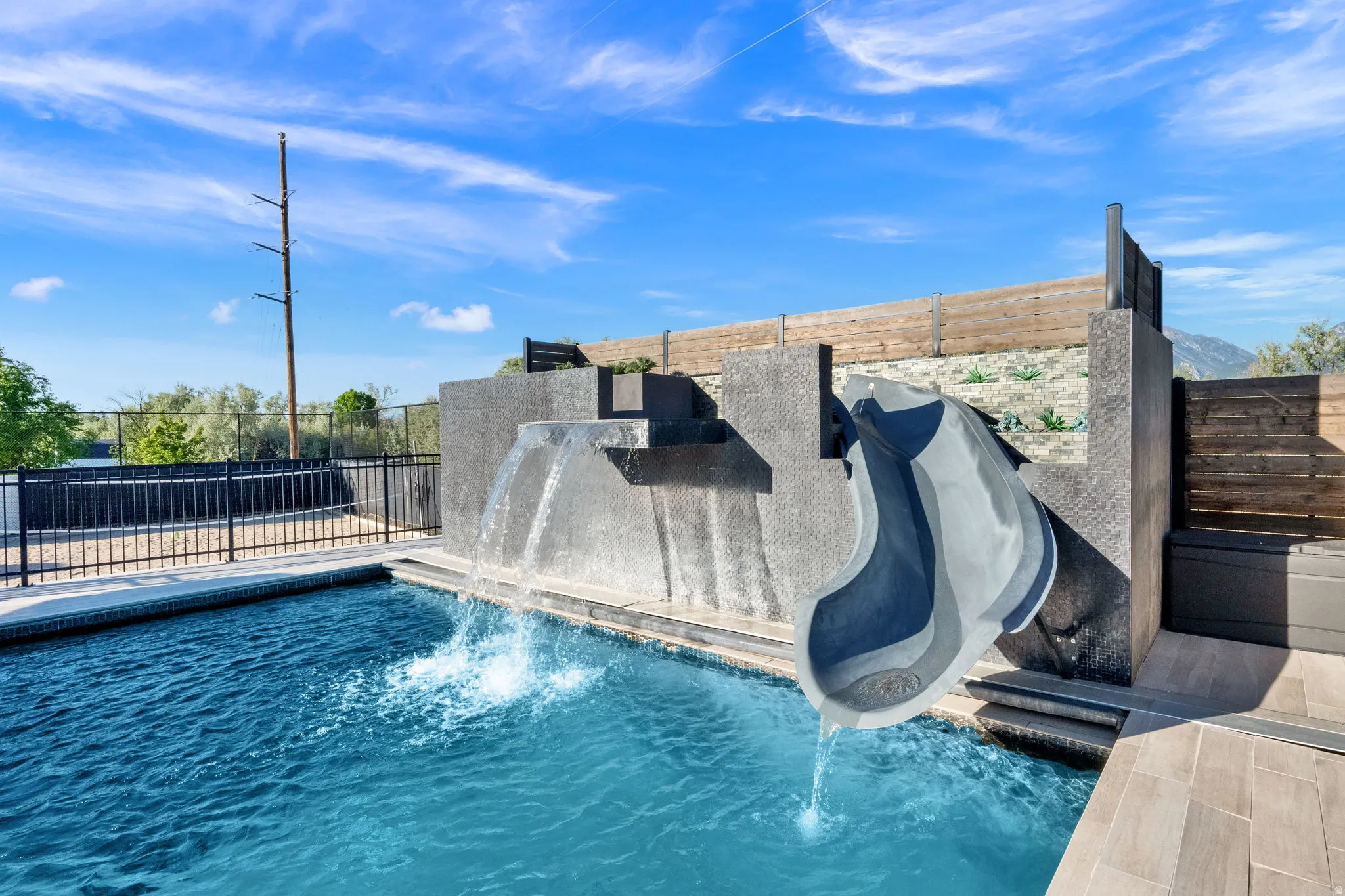 Swimming pool featuring a built-in water slide, multi-level water features, tiled pool edging, and surrounding tile decking