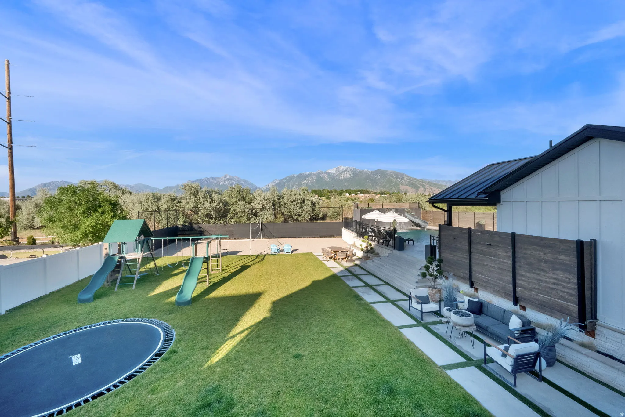 Expansive backyard featuring a manicured lawn, an in-ground trampoline, and a dedicated play structure
