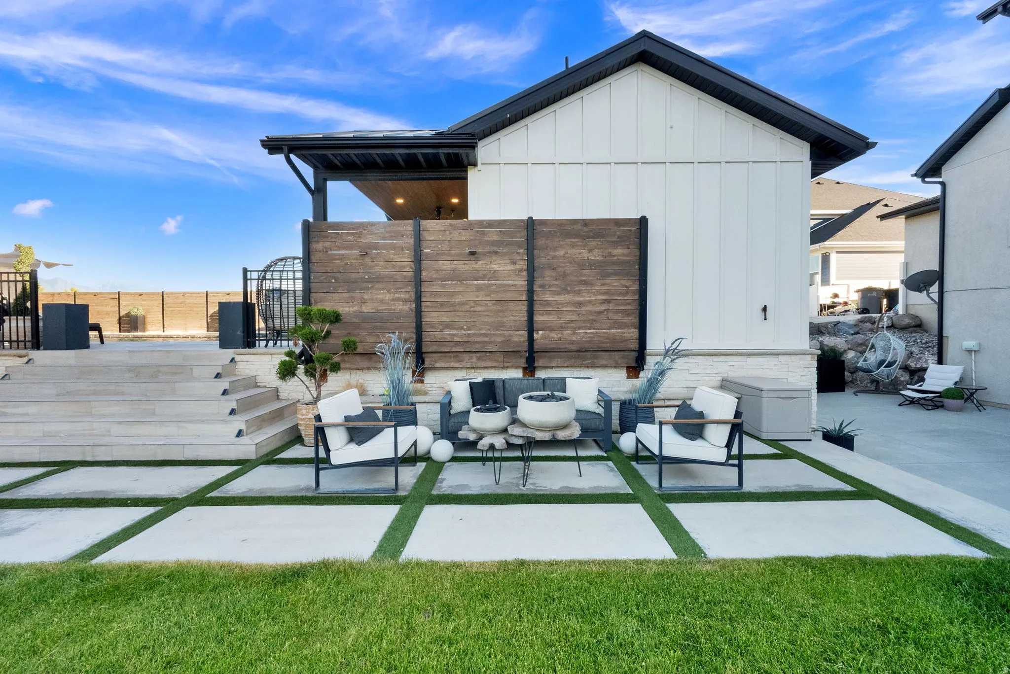 Modern exterior featuring white board-and-batten siding with black trim, a covered patio with wood paneling, and an expansive tiered hardscape patio