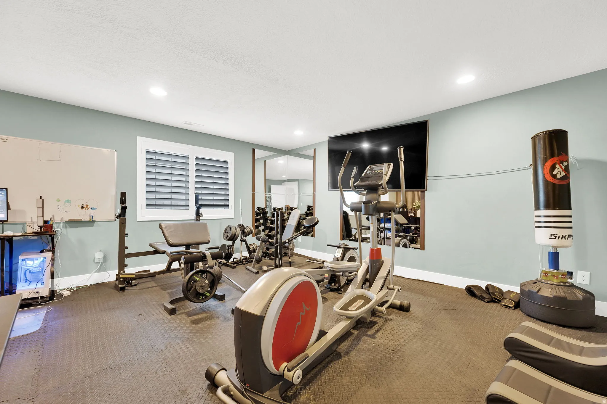 Dedicated fitness space featuring rubber flooring, recessed lighting, and a large wall-mounted display