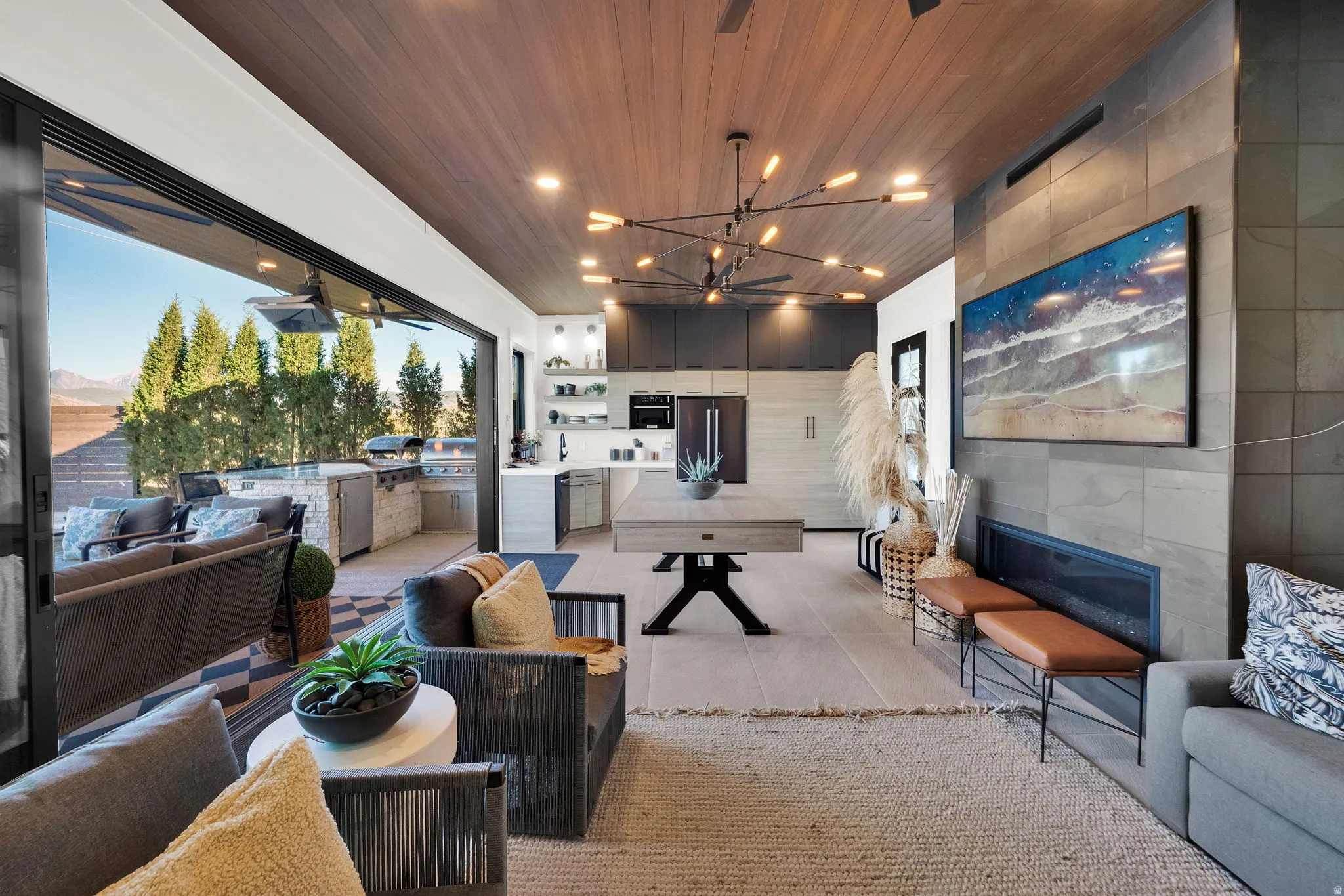 Expansive outdoor living area featuring a built-in kitchen, a large sliding glass door system, and a wood-finish ceiling with recessed lighting