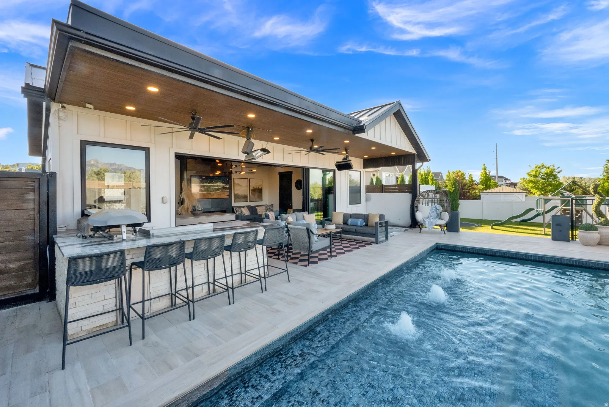 Outdoor living space featuring a swimming pool with water features, an outdoor kitchen with bar seating, and a covered patio with recessed lighting and ceiling fans