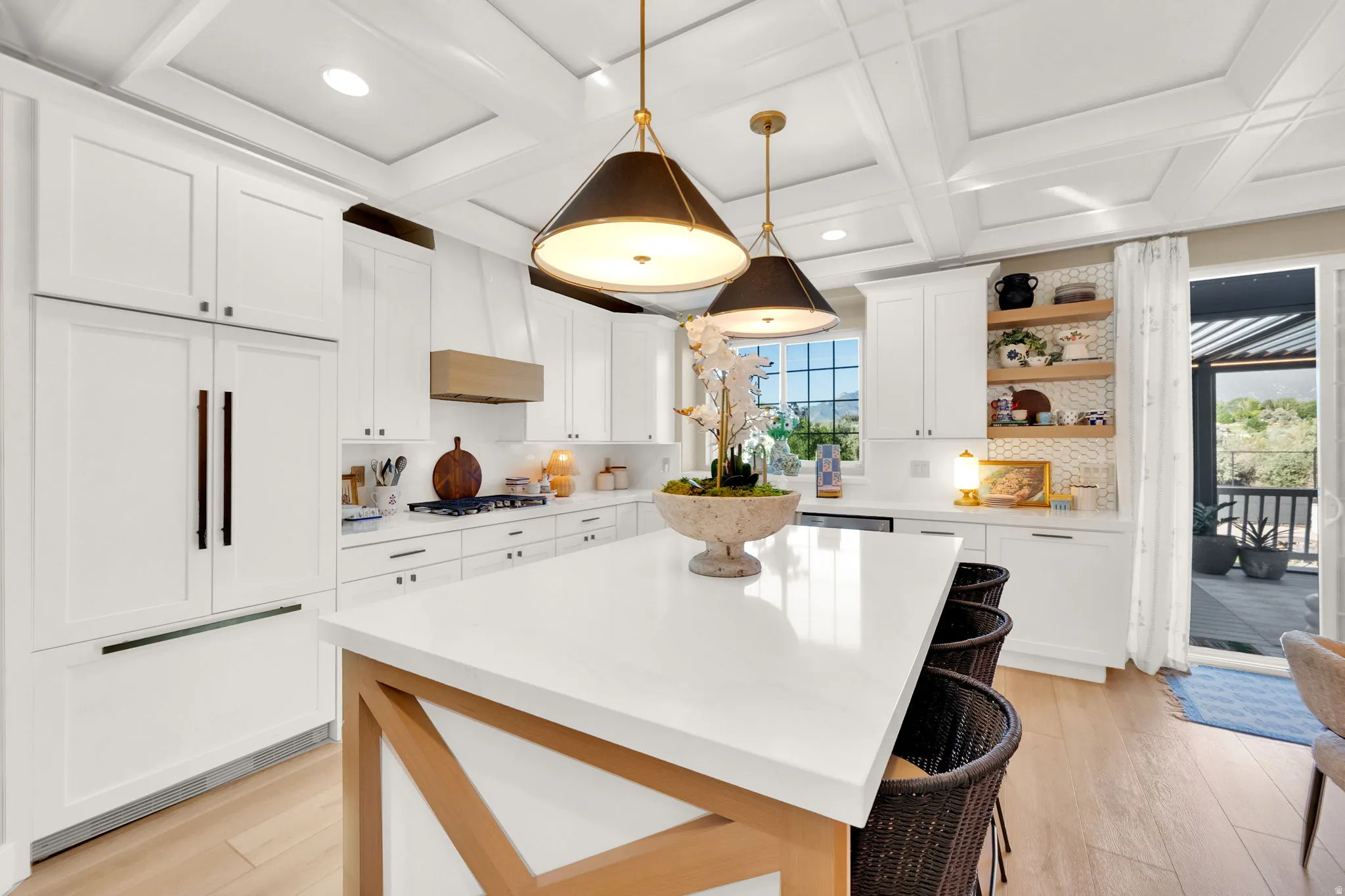 Spacious kitchen featuring white cabinetry, a large center island with seating, pendant lighting, built-in appliances, and light wood-finish flooring