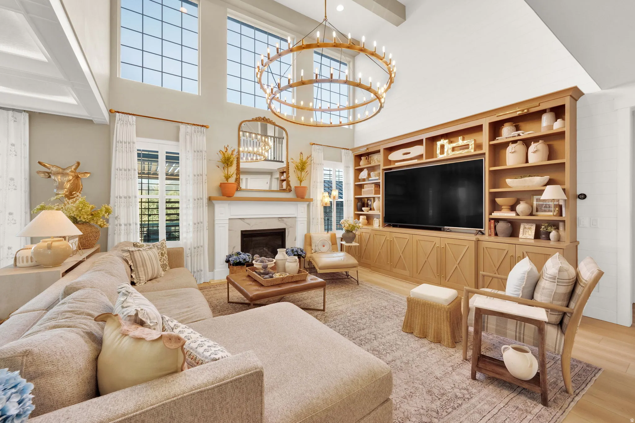Vaulted ceiling living area featuring a large brass chandelier, a built-in media center with wood-finish cabinetry, a fireplace with a mantel, and tall windows