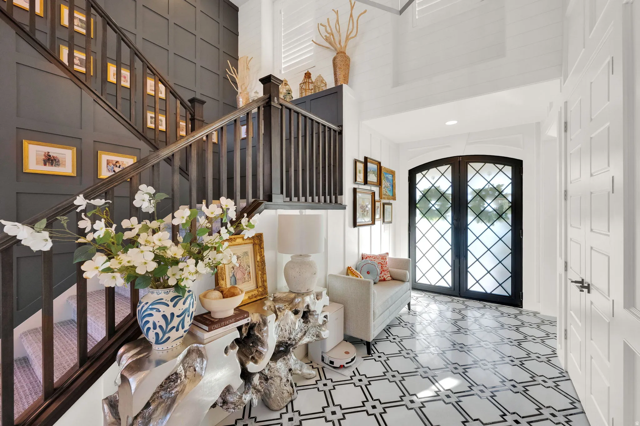 Grand foyer featuring a paneled accent wall, dark wood staircase with railing, patterned floor tile, arched French doors with diamond grilles, and shiplap wall treatment
