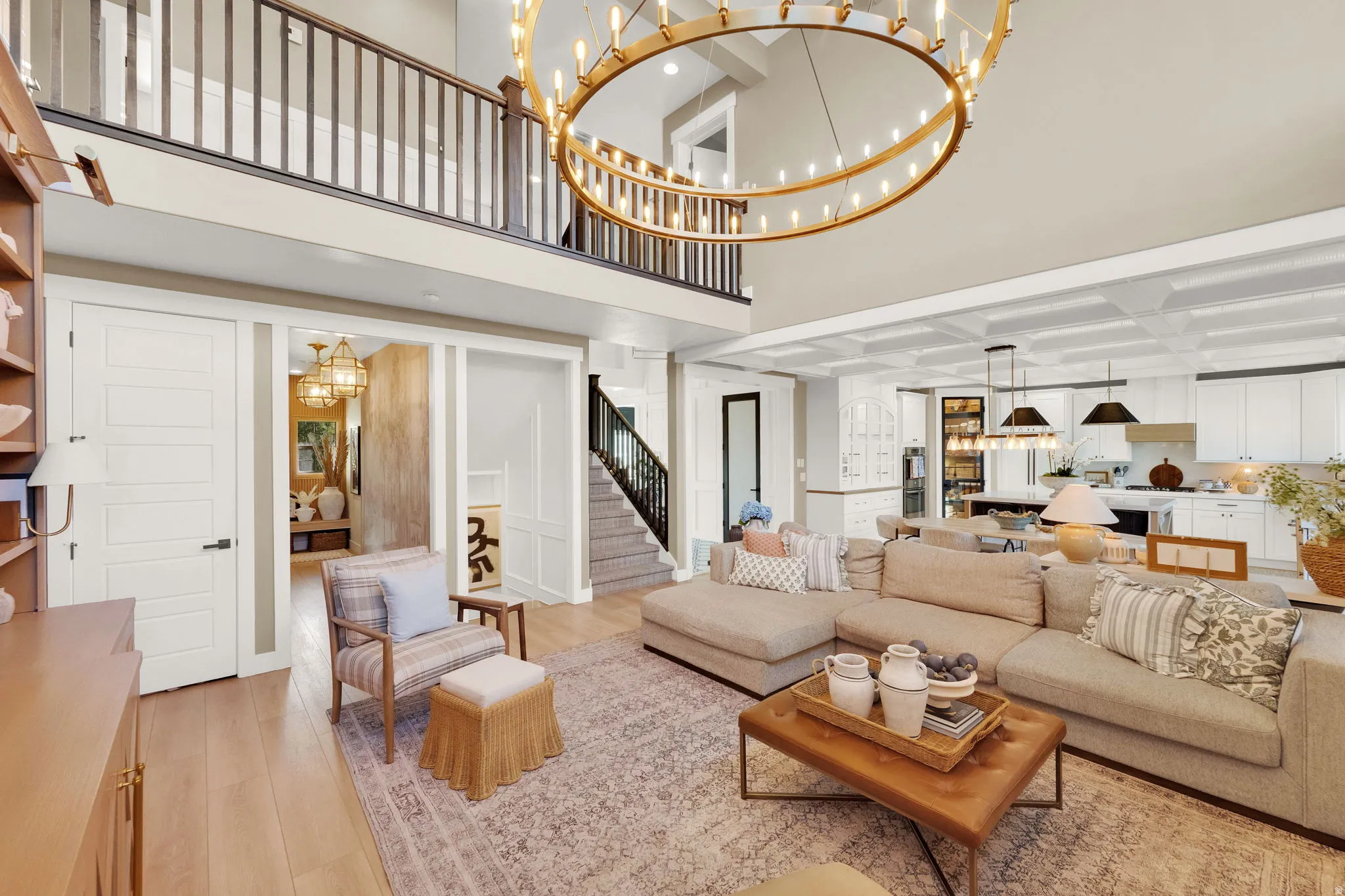 Great room featuring high ceilings, a grand circular chandelier, wood-finish flooring, a coffered ceiling, and an open-concept kitchen