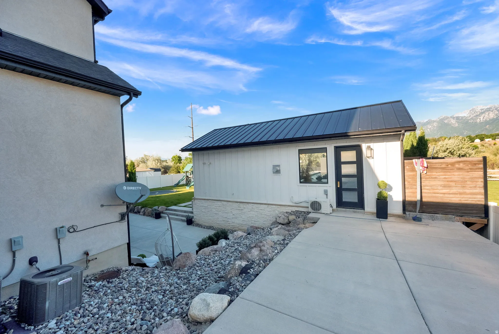 Detached accessory structure featuring a dark metal roof, white siding, and a contemporary black door with frosted glass panels