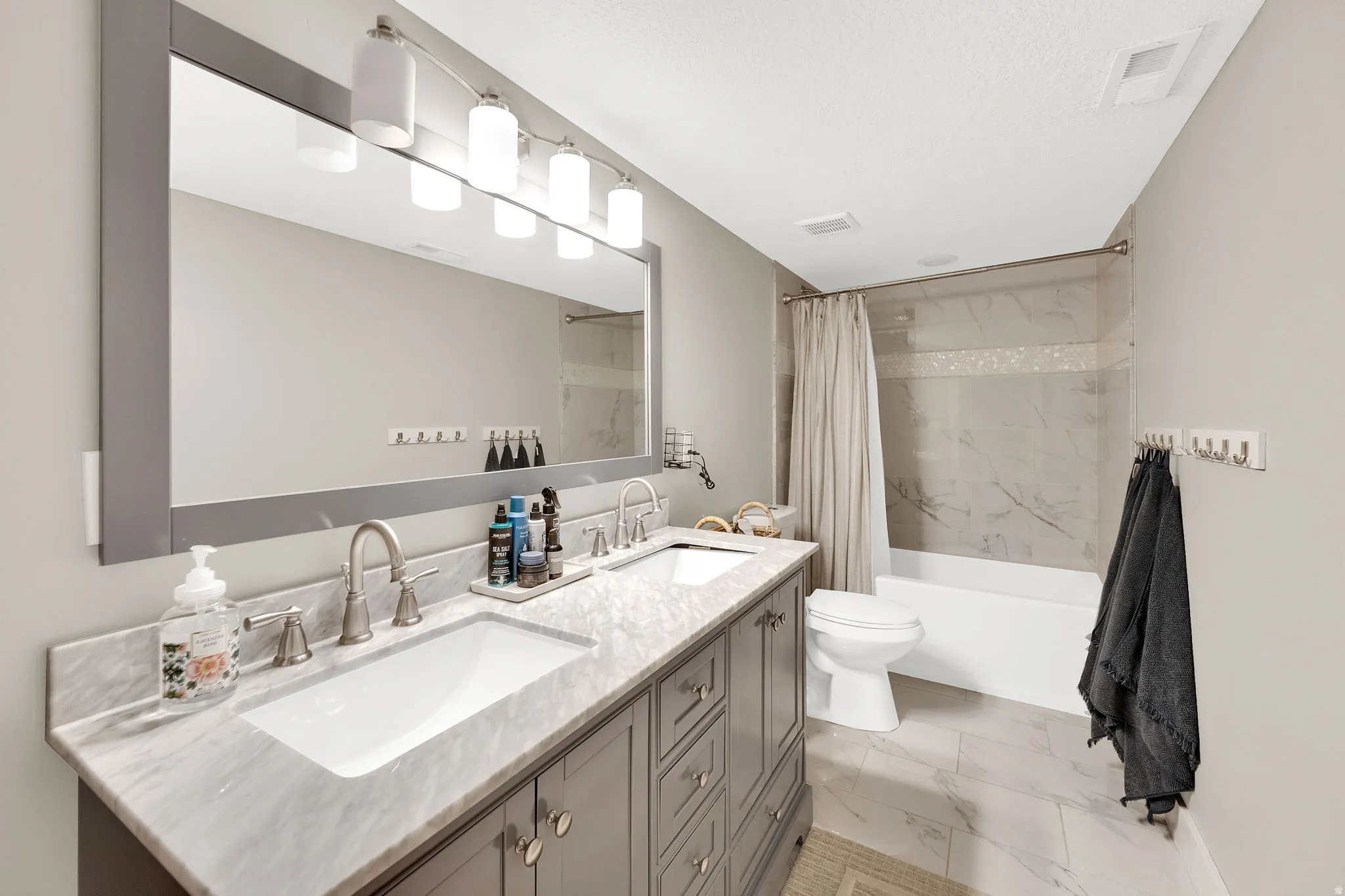 Dual basin vanity with a stone countertop, framed mirror, and contemporary lighting