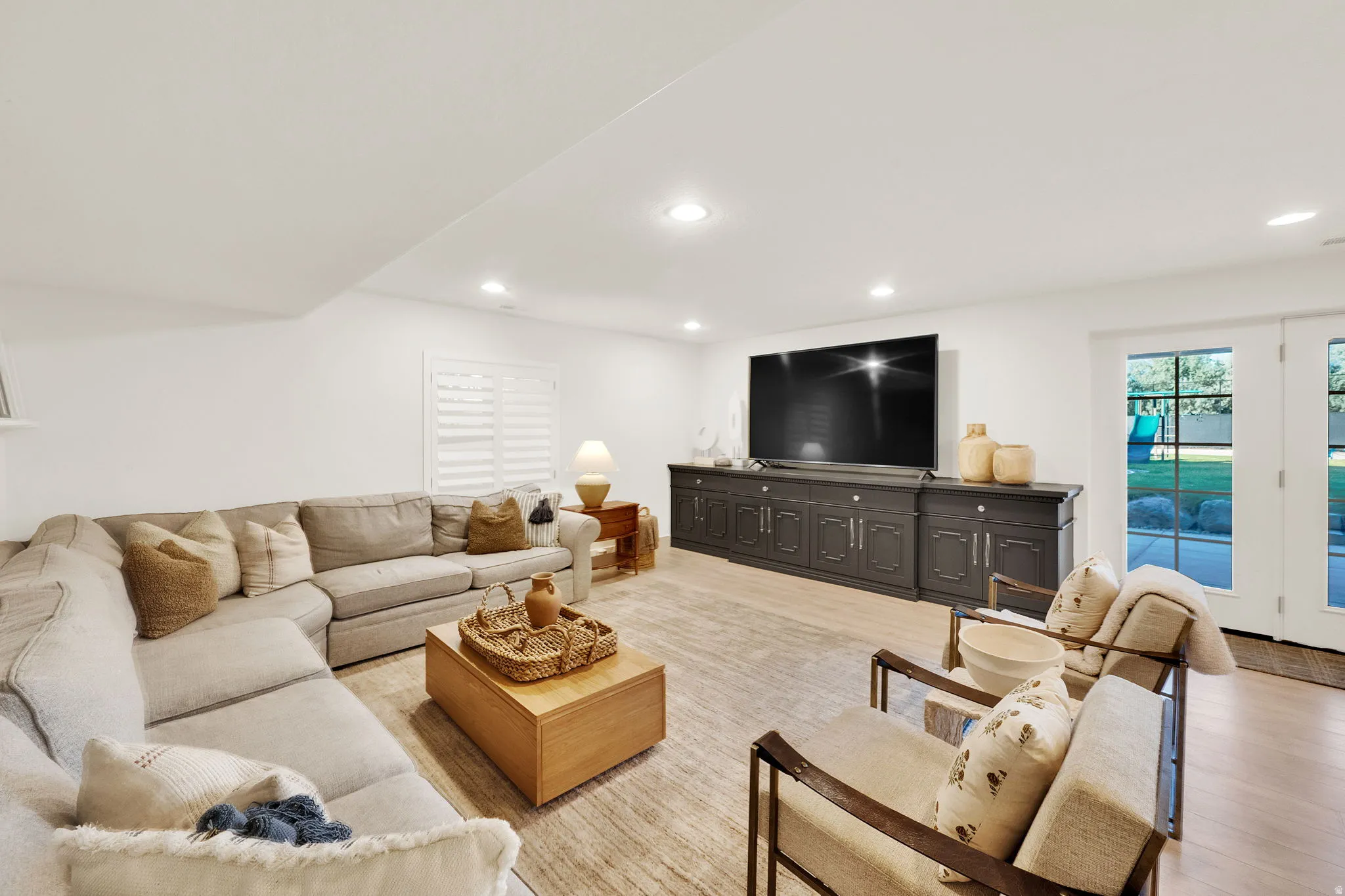 Spacious living area featuring light wood-finish flooring, recessed lighting, and white walls