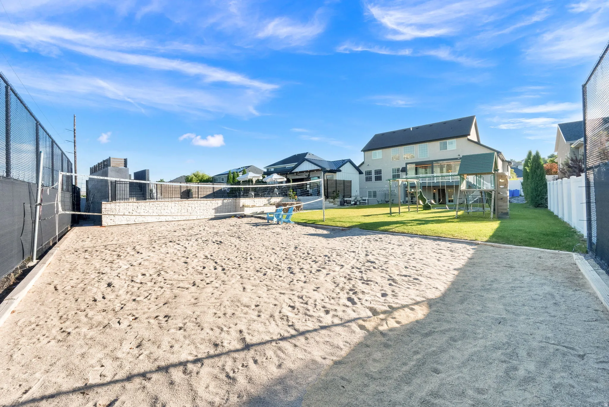 Backyard sand volleyball court with net, framed by a black chain-link fence