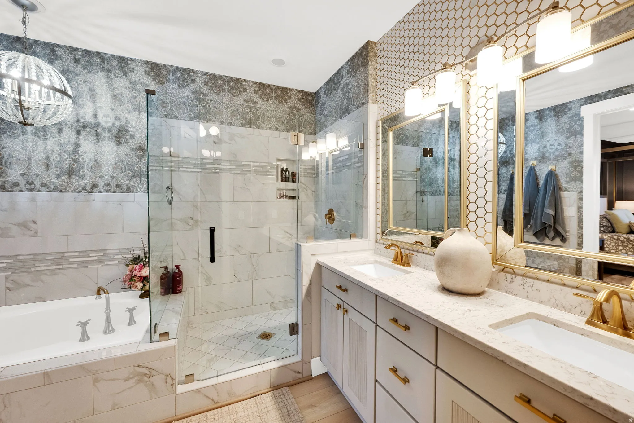 Spacious bathroom featuring a double vanity with stone countertops, an expansive walk-in shower, a built-in soaking tub, decorative wall tiling, and gold-finish fixtures