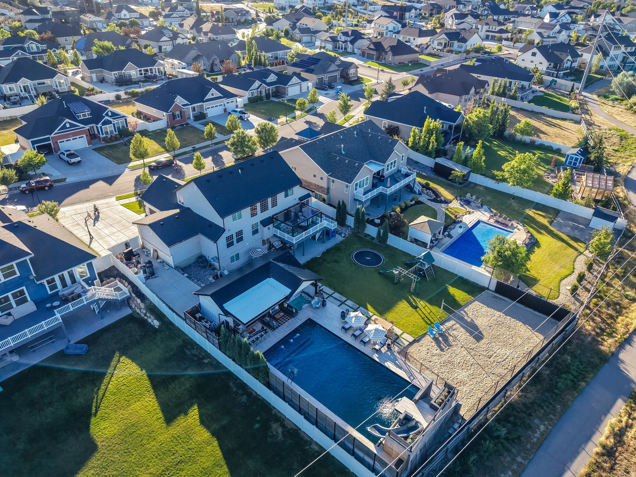 Expansive outdoor living area featuring two swimming pools, a dedicated sand court, a large grassy lawn, and multiple patio spaces