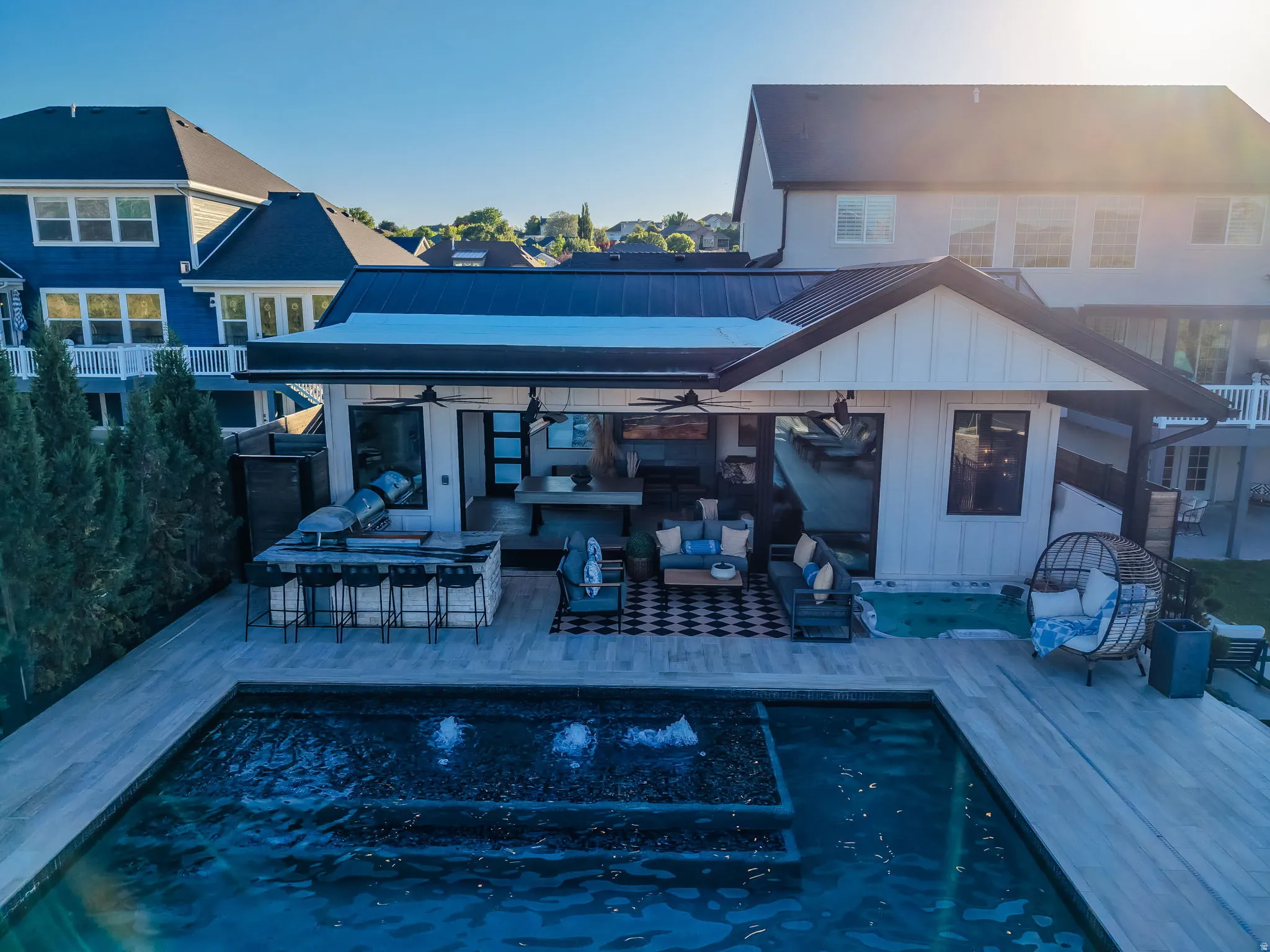 Outdoor living space featuring a swimming pool with integrated fountains, a covered patio with an outdoor kitchen, and a separate spa