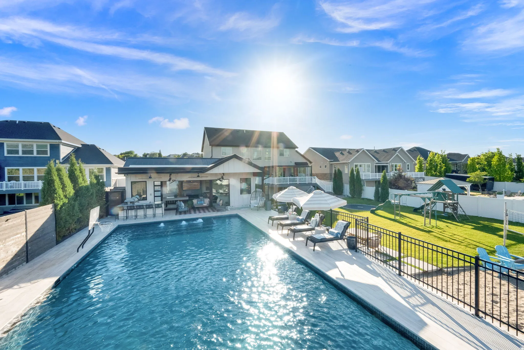 Expansive backyard featuring a rectangular swimming pool with integrated water features, an outdoor kitchen with bar seating, and a dedicated sun lounging area