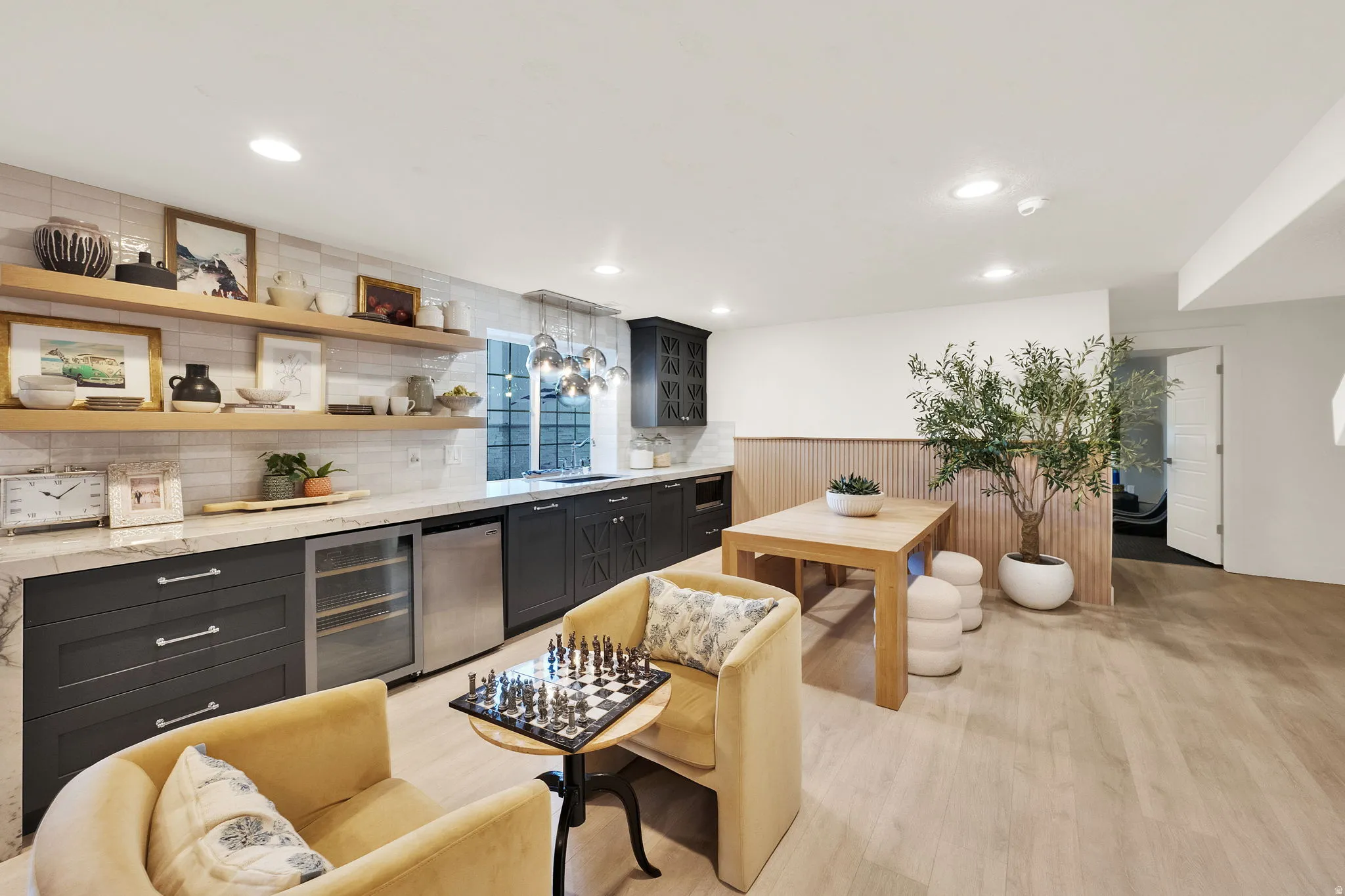 Recessed lighting illuminates a well-appointed kitchen area featuring dark cabinetry, a beverage refrigerator, and a light-toned countertop