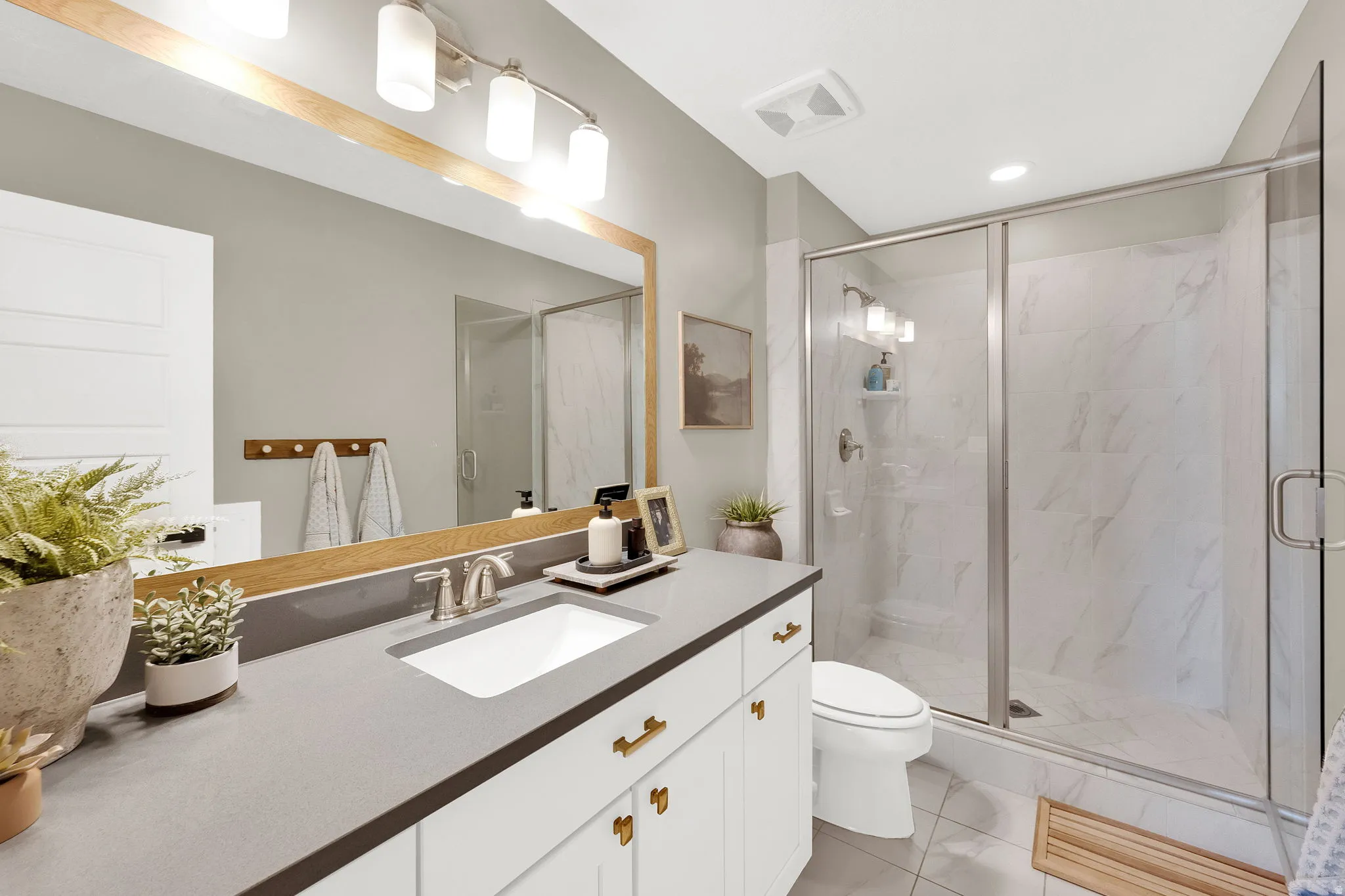 Bathroom featuring a single vanity with a gray countertop, white cabinetry with brass hardware, and a framed mirror