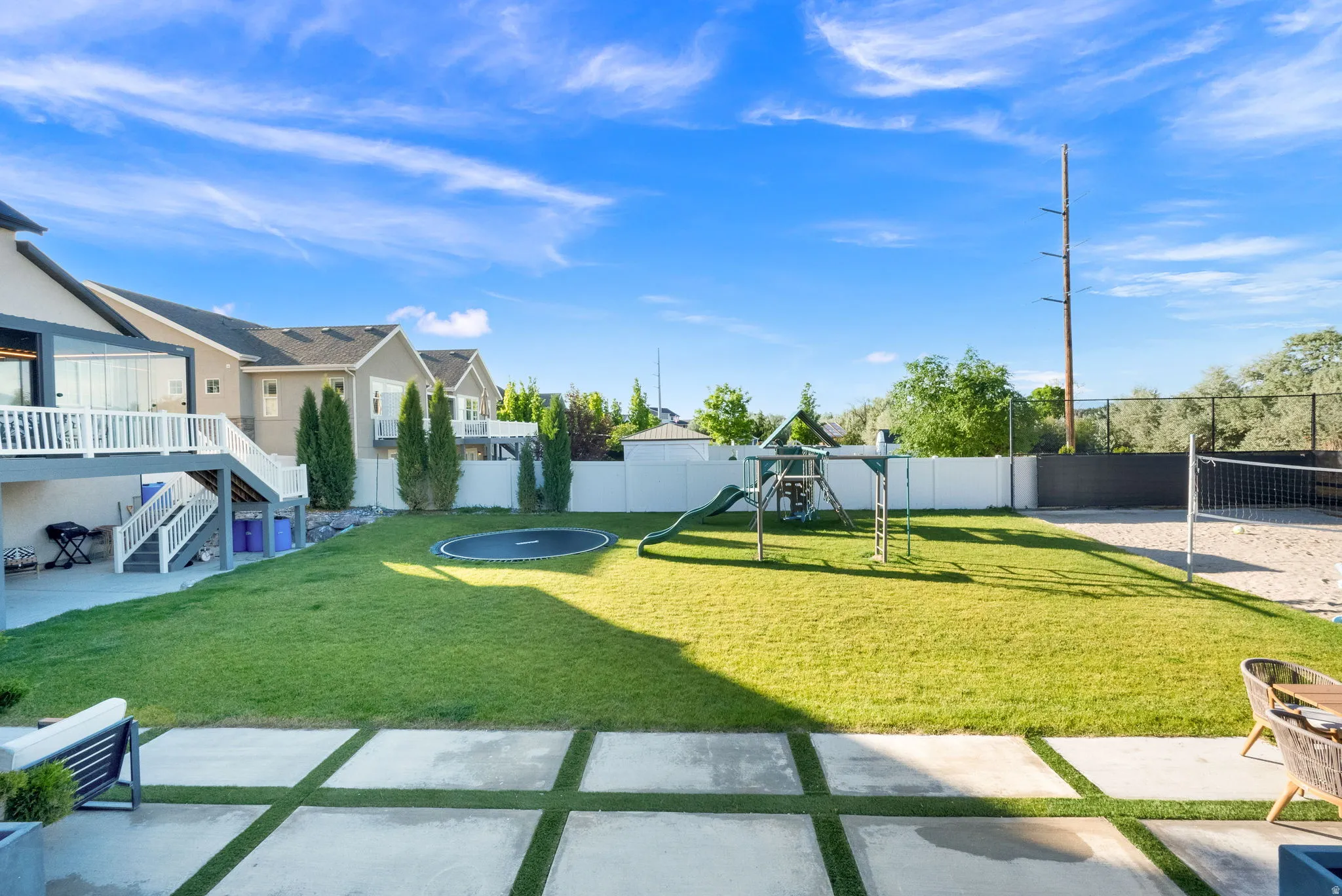 Expansive backyard featuring a lush lawn, concrete patio with grass inserts, and a dedicated sand volleyball court