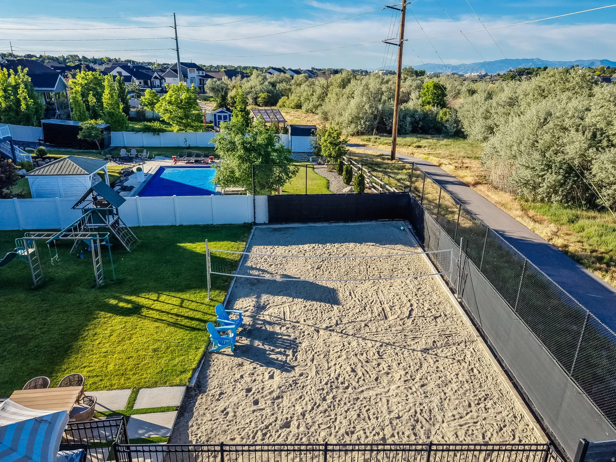 Expansive outdoor space featuring a sand volleyball court, manicured lawn, and a fenced swimming pool