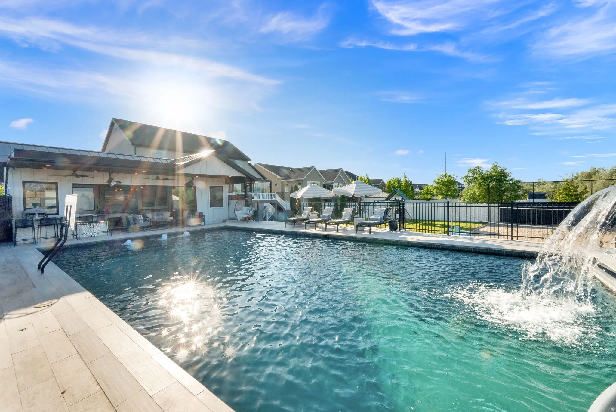 Expansive outdoor pool area featuring a built-in pool with water features, surrounding patio, and a covered outdoor living space