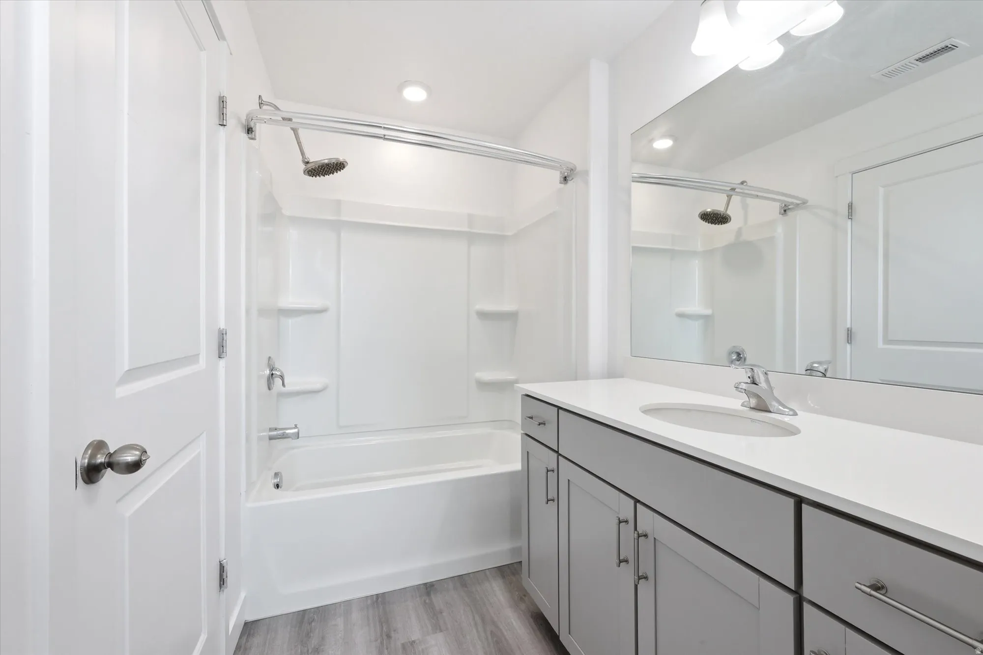 Full bathroom featuring a white tub/shower combination, light gray wood-finish flooring, a white countertop vanity with gray cabinetry, an integrated sink, and a large wall-mounted mirror