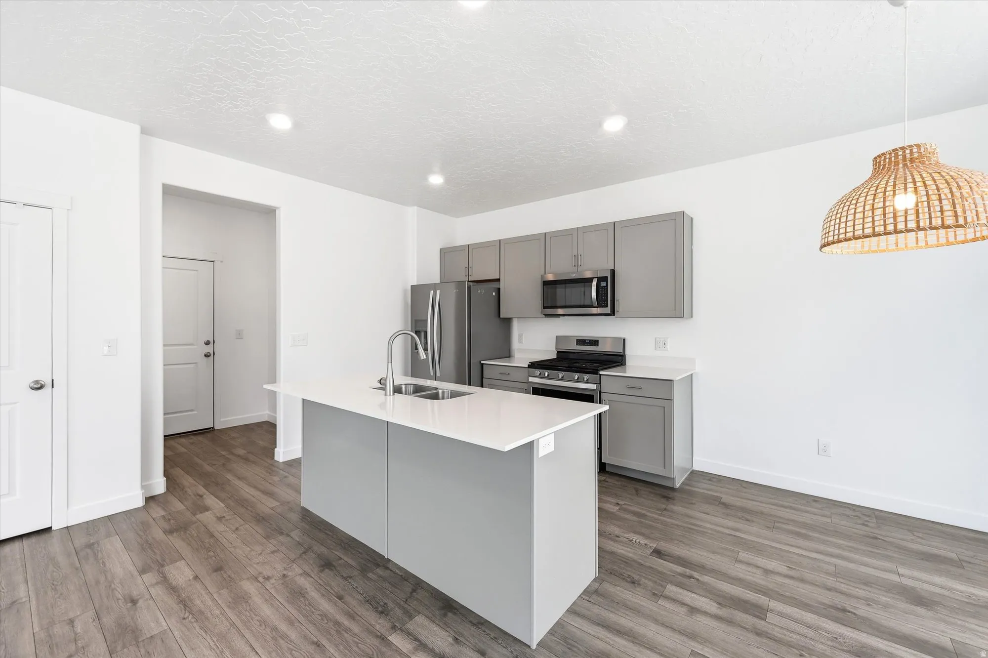 Contemporary kitchen featuring a center island with sink, stainless steel appliances, gray cabinetry, and wood-finish flooring