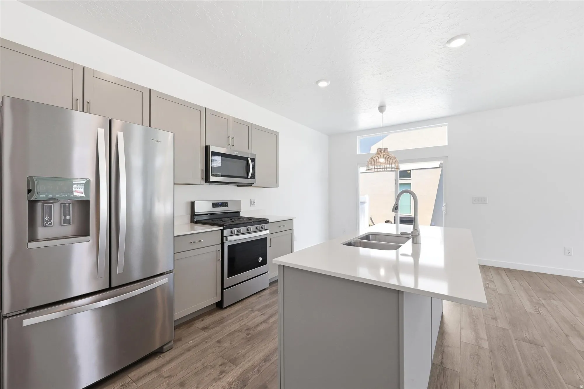 Kitchen featuring stainless steel appliances, light gray cabinetry, and a central island with a double basin sink