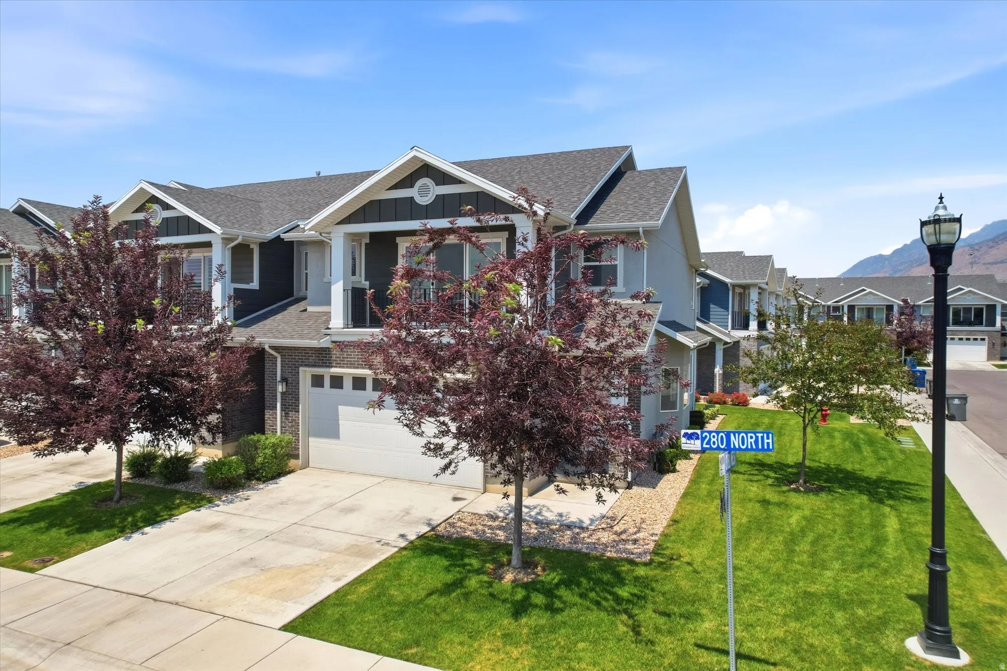 Contemporary townhome featuring a two-car garage, private driveway, and mature landscaping