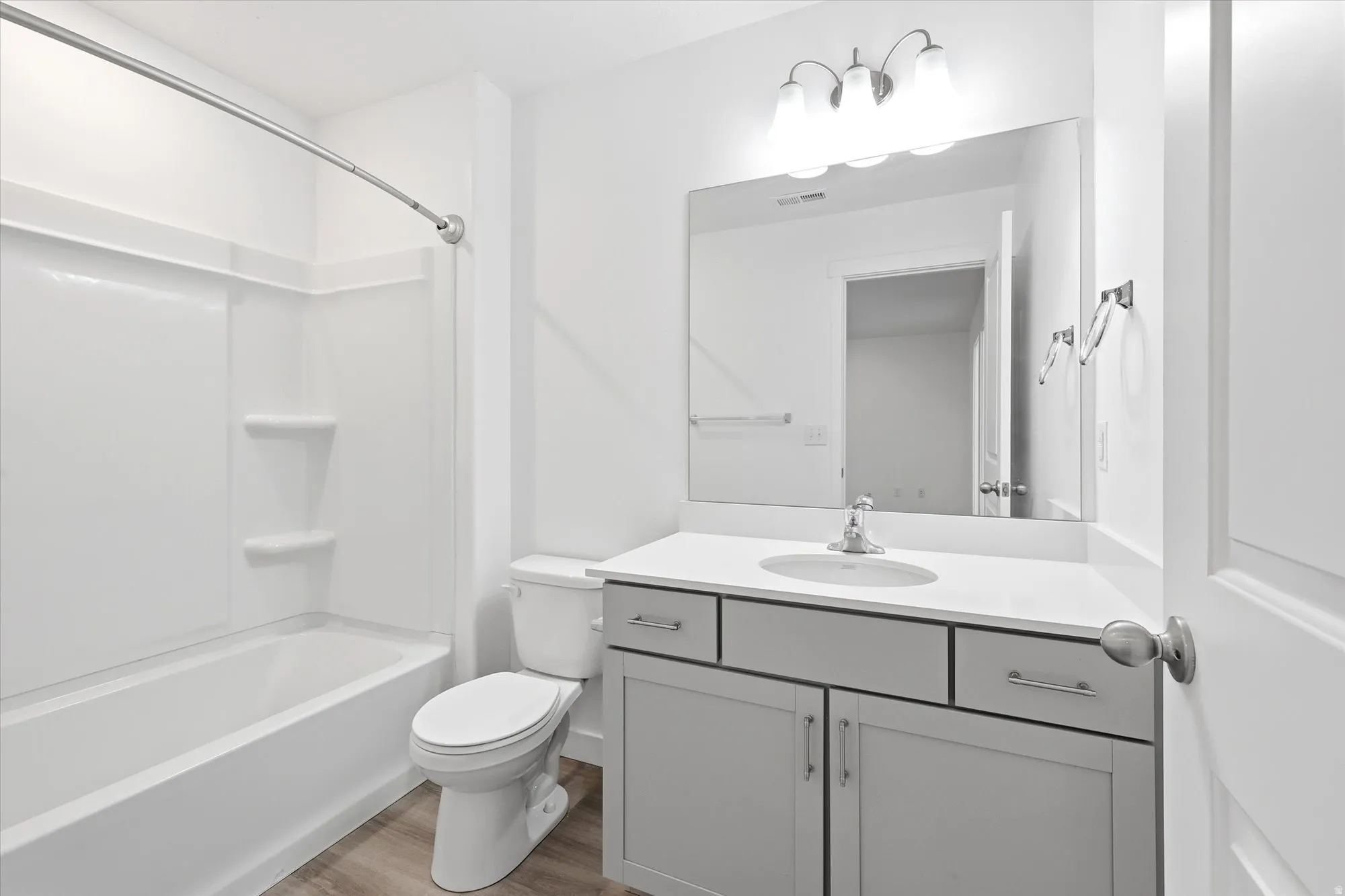 Bathroom featuring a single vanity with quartz-style countertop, white cabinetry with silver hardware, a large wall-mounted mirror, and a white tub and shower combination with an integrated shelving system