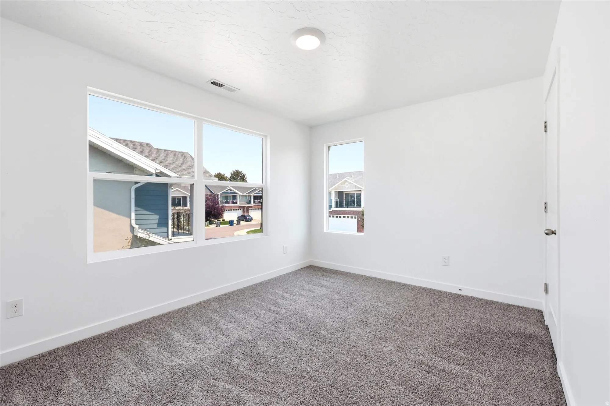 Bright room with a large multi-pane window, secondary window, white walls, and gray patterned carpet